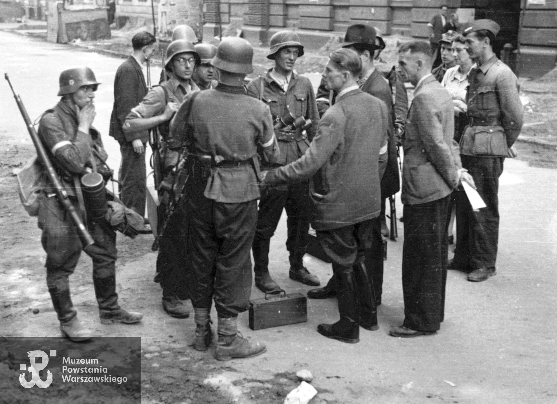 Fotografia z Powstania Warszawskiego. Śródmieście Północne. Grupa Powstańców z kompanii "Koszta" rozmawiająca na ulicy Moniuszki. Stoją od lewej: kpr. Andrzej Ferencowicz "Siuchaj", st. strz. Tadeusz Suliński "Radwan", plut. pchor. Jerzy Tyczyński "Jur"; tyłem stoją: plut. pchor. Włodzimierz Radajewski "Rataj", por. Roman Rozmiłowski "Zawada". Widoczni na zdjęciu od prawej strony: Stanisław Grochowski „Stanisław”, mjr Tadeusz Grochowski ps. "Fidelis" . Ujęcie w kierunku południowo-wschodnim. W tle widoczny fragment kamienicy nr 9 i 7 (po lewej). Kapral  Stanisław Grochowski  (w furażerce) - identyfikacja w oparciu o informacje p. Zofii Szmid, córki Wandy Regenciak - Grochowskiej - Święcińskiej. Autorem zdjęcia jest Eugeniusz Lokajski ”Brok". Fot. ze zbiorów Muzeum Powstania Warszawskiego, sygn. MPW-IP/759