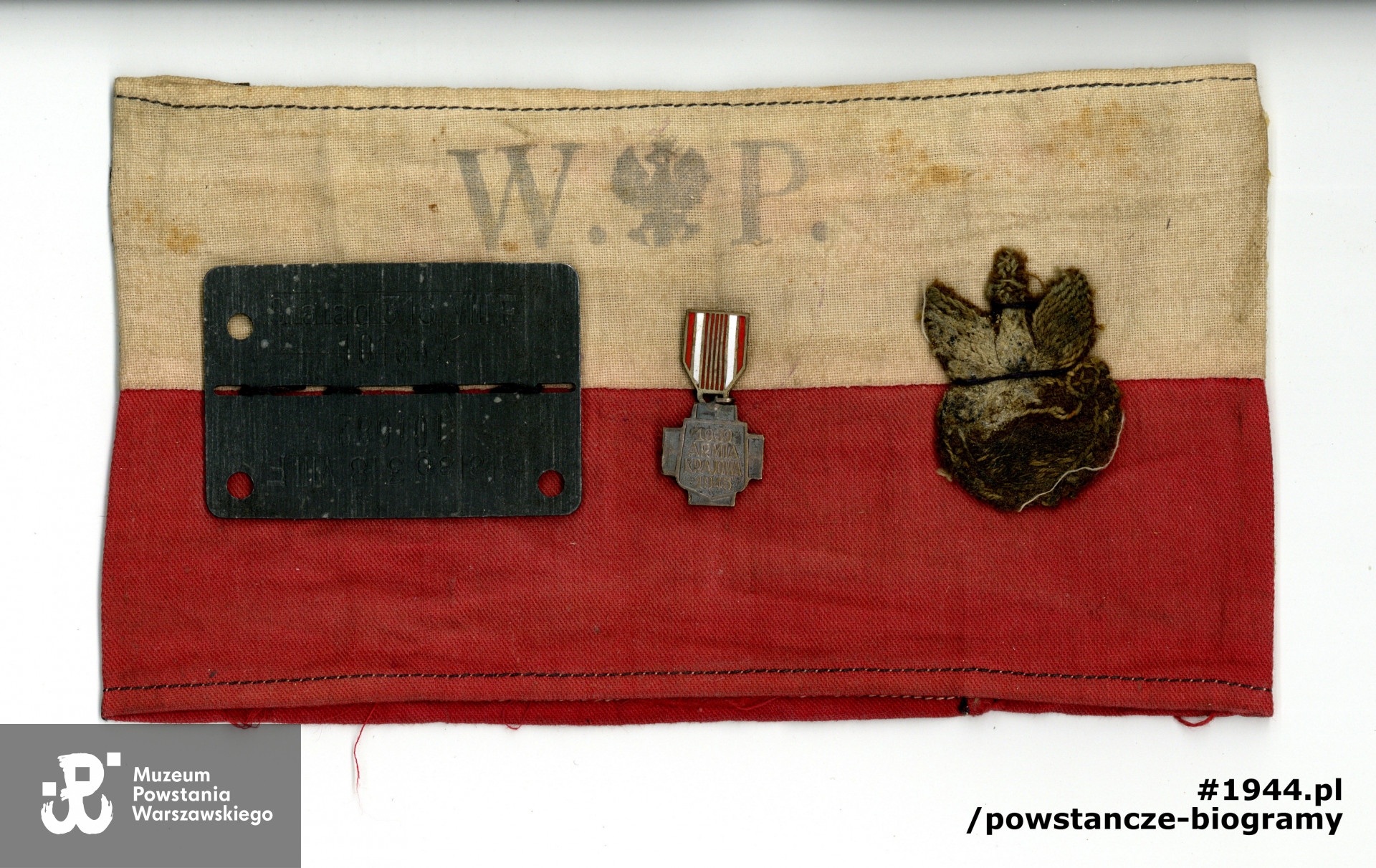 Należąca do ppor. Stanisława Chmielowskiego opaska z okresu Powstania Warszawskiego. Do materiału przypięto po wojnie m. in. blaszkę jeniecką oraz miniaturę Krzyża AK. Z archiwum rodzinnego, udostępniła p. Anna Chmielowska - Łachwa
