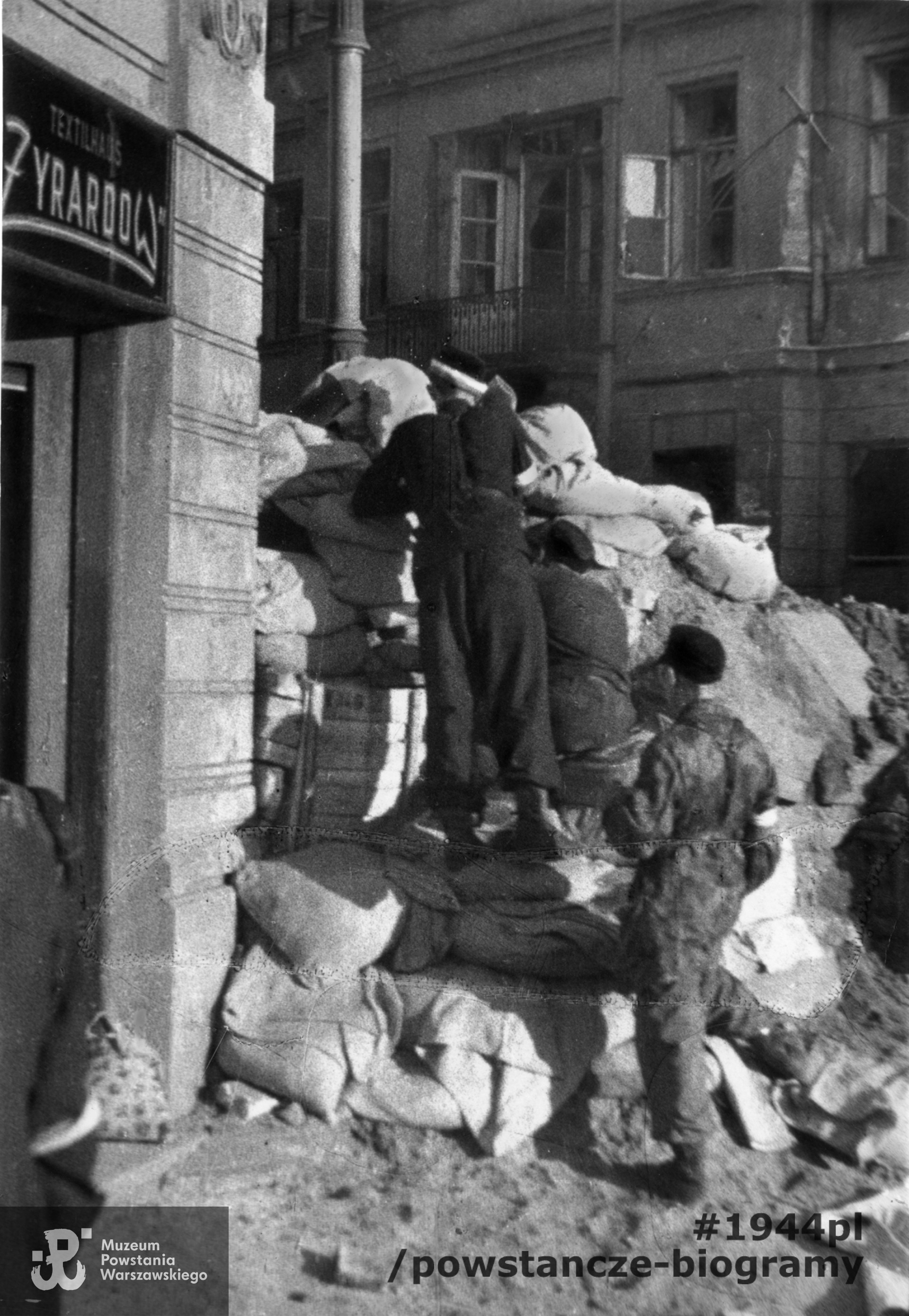 Fotografia z Powstania Warszawskiego Starówka. Powstańcy na barykadzie "Żyrardów", zwanej też redutą "św. Trójcy" przegradzającej ul. Bielańską na wysokości wylotu ul. Daniłowiczowskiej. W tle po prawej widoczny fragment elewacji dawnego Hotelu Lipskiego przy ul. Bielańskiej 3. Autorem zdjęcia jest Józef Jerzy Karpiński. Fot. ze zbiorów Muzeum Powstania Warszawskiego, sygn. MPW-IP/6482