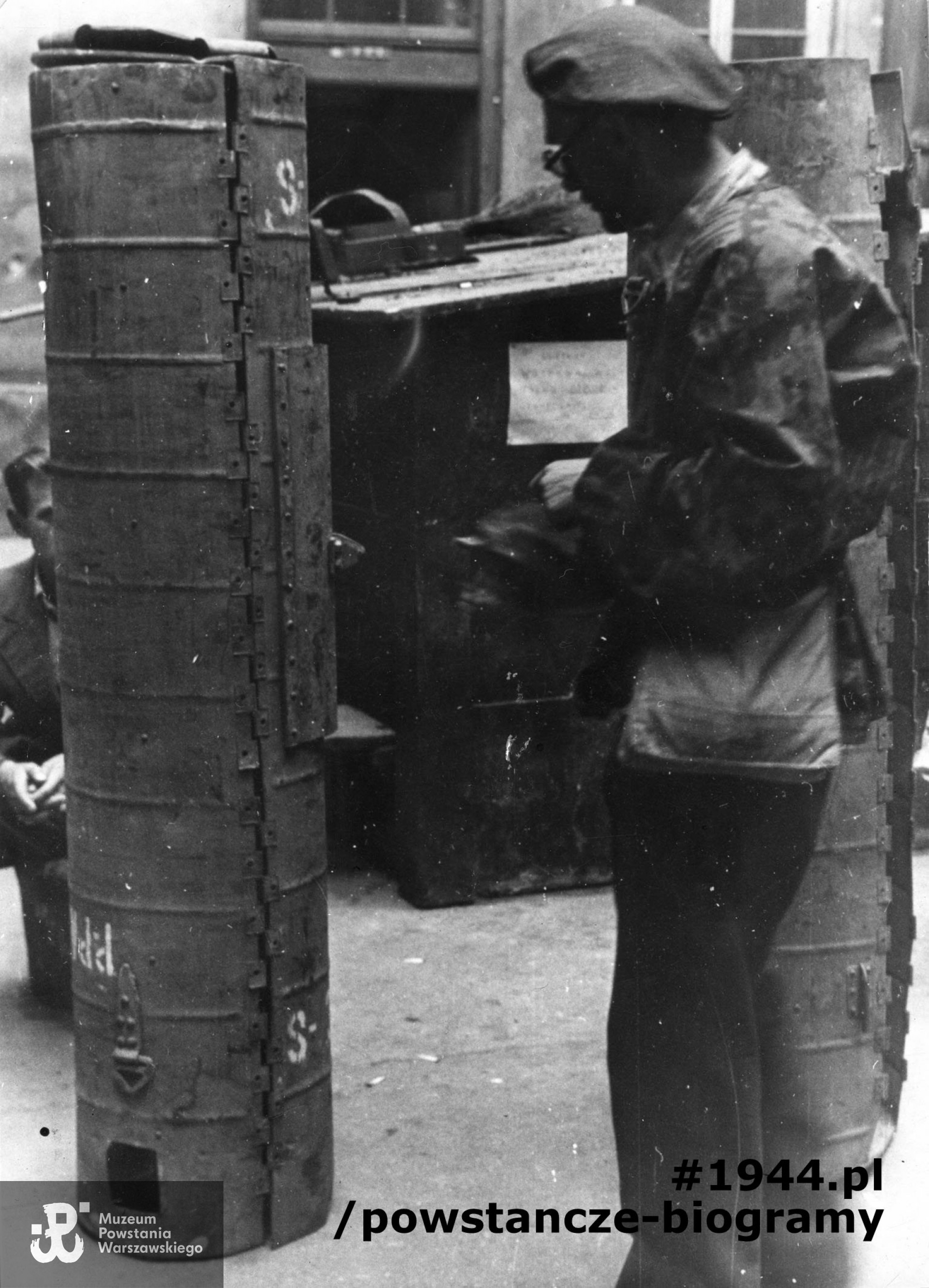 Fotografia z Powstania Warszawskiego. Powiśle. Jerzy Zarzycki "Pik", szef operatorów filmowych, przygląda się zasobnikowi zrzutowemu na podwórzu kamienicy przy ul. Tamka 46. Fot. ze zbiorów Muzeum Powstania Warszawskiego, sygn. MPW-IK/2635