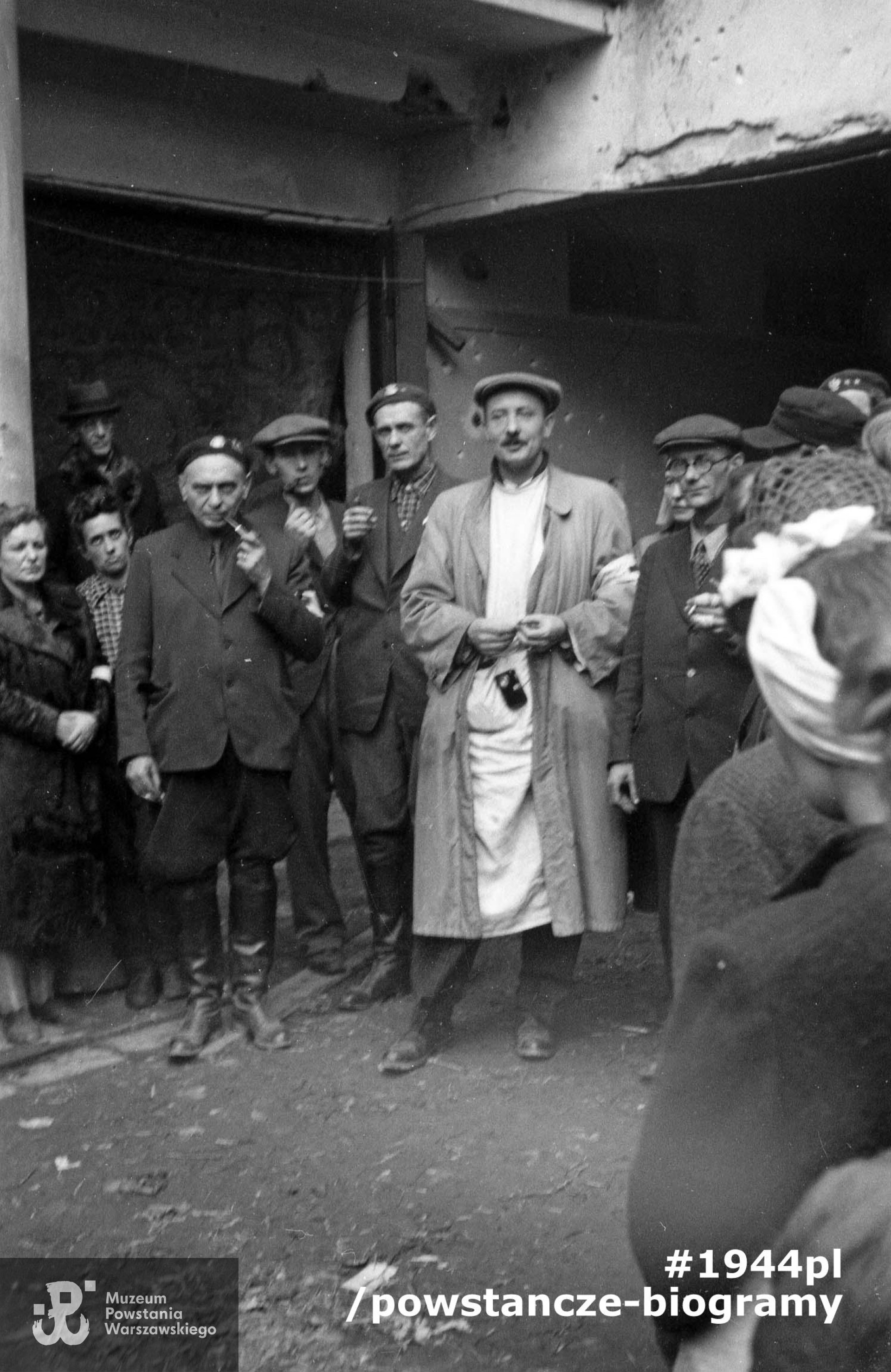 Fotografia z Powstania Warszawskiego. Podwórze szpitala polowego przy Wspólnej 27. Grupa lekarzy w otoczeniu współpracowników. W środku w białym kitlu mjr dr Feliks Michalec "Doktór Piotr", po jego prawej kpt. dr Tadeusz Gerwel "Orda" i ppłk dr Tadeusz Bętkowski "Tata" (z fajką). Fot. ze zbiorów Muzeum Powstania Warszawskiego, sygn. MPW-IN/3771