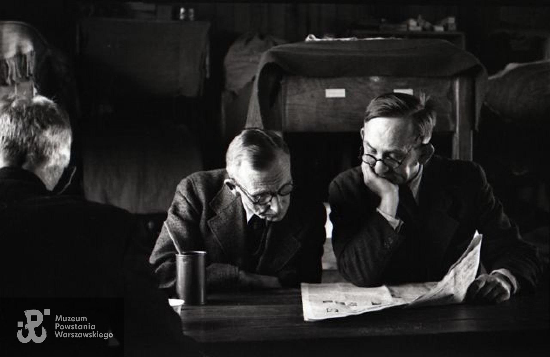 Fotografia z Polskiego Szpitala Wojskowego w saksońskim Zeithain. Barak nr 14. Mjr dr Michał Grobelski "Doktor Zygmunt" (z lewej) i dr Mieczysław Zapolski podczas lektury niemieckiej gazety. Z lewej, odwrócony, mjr dr Tadeusz Kawecki " Lwowicz". Fot. ze zbiorów Muzeum Powstania Warszawskiego, sygn. MPW-IN/3788