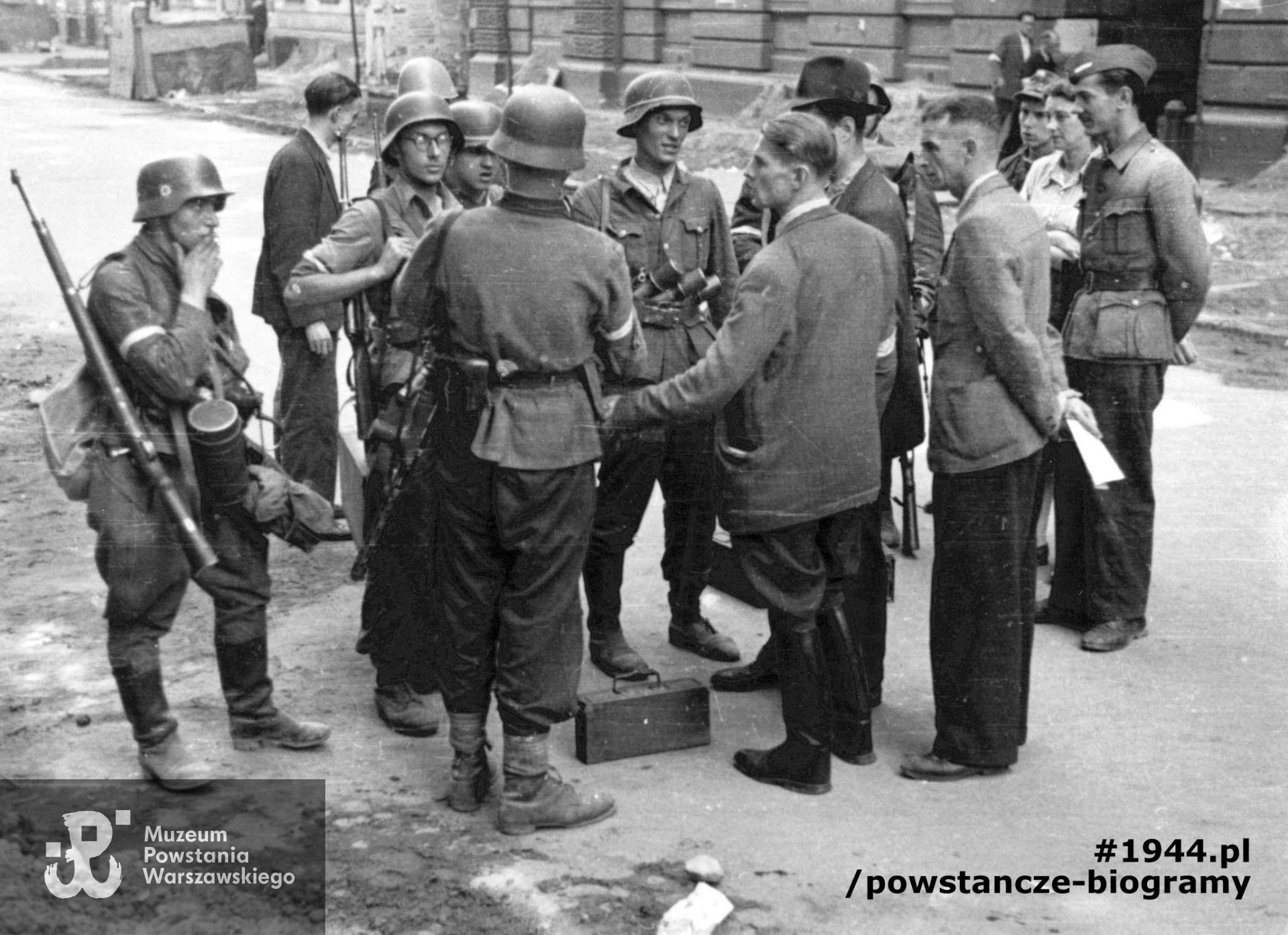 Fotografia z Powstania Warszawskiego. Śródmieście Północne. Grupa Powstańców z kompanii "Koszta" rozmawiająca na ulicy Moniuszki. Stoją od lewej: kpr. Andrzej Ferencowicz "Siuchaj", st. strz. Tadeusz Suliński "Radwan", plut. pchor. Jerzy Tyczyński "Jur"; tyłem stoją: plut. pchor. Włodzimierz Radajewski "Rataj", por. Roman Rozmiłowski "Zawada". Widoczni na zdjęciu od prawej strony: Stanisław Grochowski „Stanisław”, mjr Tadeusz Grochowski ps. "Fidelis" . Ujęcie w kierunku południowo-wschodnim. W tle widoczny fragment kamienicy nr 9 i 7 (po lewej). Kapral  Stanisław Grochowski  (w furażerce) - identyfikacja w oparciu o informacje p. Zofii Szmid, córki Wandy Regenciak - Grochowskiej - Święcińskiej. Autorem zdjęcia jest Eugeniusz Lokajski ”Brok". Fot. ze zbiorów Muzeum Powstania Warszawskiego, sygn. MPW-IP/759