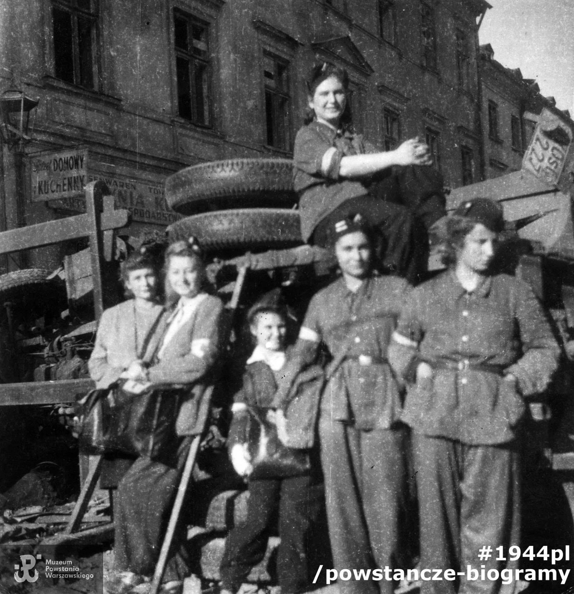 Sanitariuszki 3 plutonu kompanii szturmowej batalionu "Kiliński" przy barykadzie na wysokości styku domów Grzybowska 16 i 14 (elewacja widoczna w tle). Od lewej sanitariuszki: Krystyna Świder "Lena", Maria Rosołowska "Ewa Mostowicz", Krystyna Borysławska "Maria Jolanta", Jadwiga Włodarska "Jadzia", patrolowa: Halina Szulakowska "Irma", łączn. Aleksandra Zaborowska "Oleńka". Fotografia ze zbiorów Muzeum Powstania Warszawskiego sygnatura MPW-IP/2078