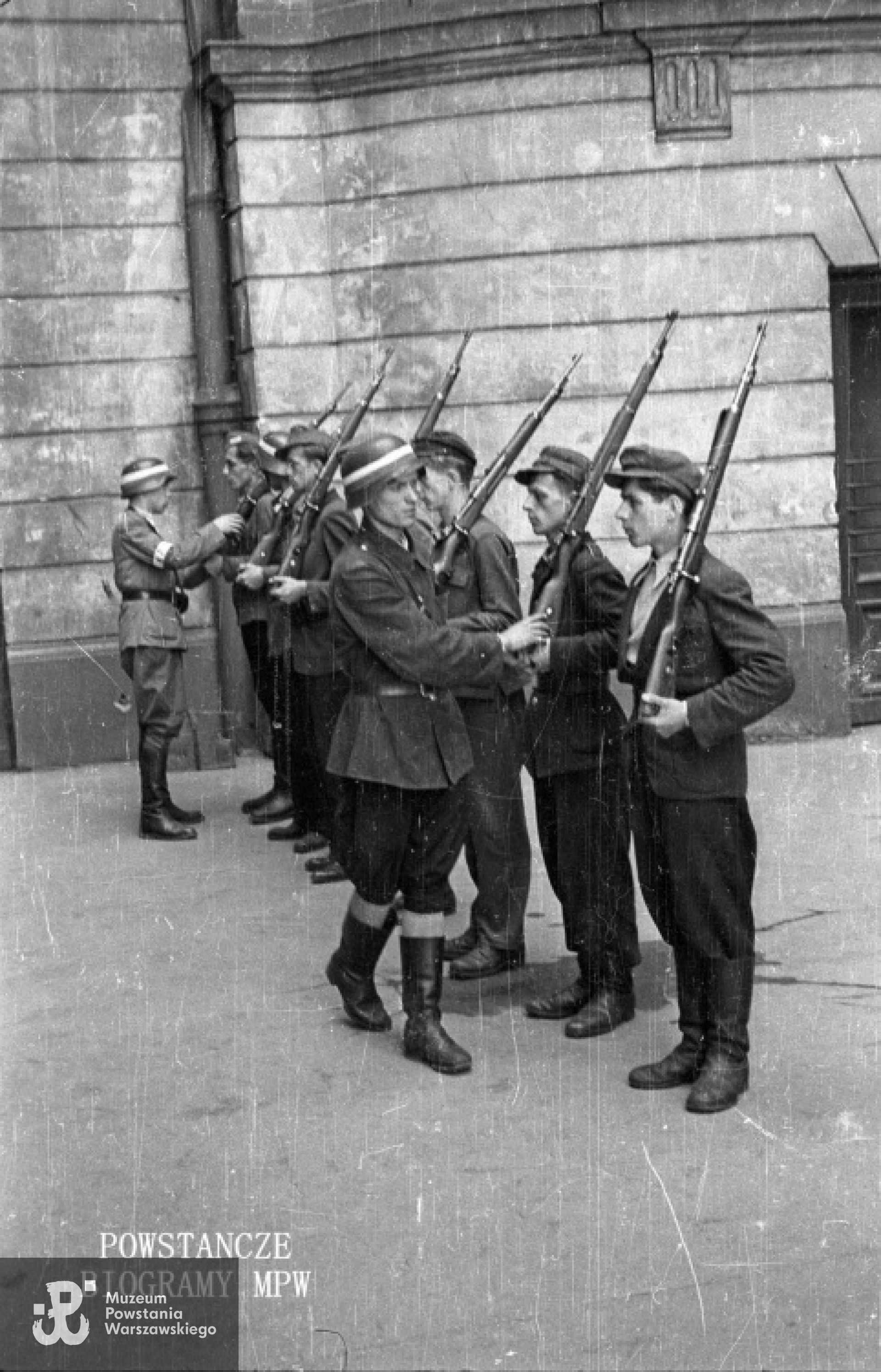 Fotografia z Powstania Warszawskiego. Śródmieście Północne. Musztra 3. drużyny I plutonu kompanii "Koszta" na podwórzu kamienicy przy Moniuszki 12; drugi od prawej: pchor. Ryszard Ryng "Dick", trzeci st. strz. pchor. Tadeusz Szmigiera "Wład"; przed szeregiem żołnierzy stoi plut. pchor. Jerzy Tyczyński „Jur”.Fot. autorstwa Eugeniusza Lokajskiego ps. "Brok". Ze zbiorów Muzeum Powstania Warszawskiego, sygn. MPW-IN/48.