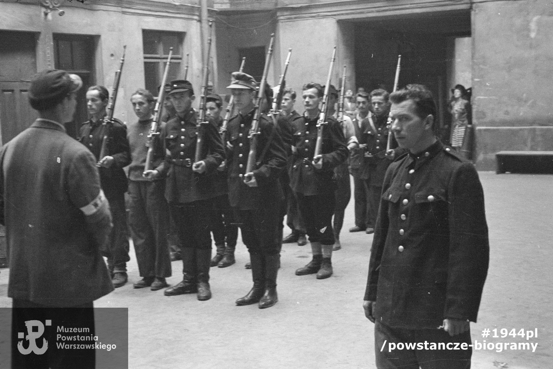 Fotografia z Powstania Warszawskiego. Śródmieście Północne. Musztra II plutonu kompanii "Koszta" na podwórzu kamienicy Jankowskiego przy ul. Moniuszki 12. Przed frontem plutonu (odwrócony tyłem) stoi ppor. Stanisław Kuśpit "Kruk", nieopodal niego stoi prowadzący musztrę plut. Edmund Klimaszewski "Jerzy"; w pierwszej czwórce od prawej: strz. Paweł Kowalczyk "Andrzej", st. strz. . Tadeusz Jankowski "Owa", st. strz. Zdzisław Kamiński "Czarny", strz. Stanisław Zieliński "Zielony"; w drugiej czwórce: pierwszy od prawej st. strz.  Henryk Gędziorowski "Henryk".  Autorem zdjęcia jest Eugeniusz Lokajski. Fot. ze zbiorów Muzeum Powstania Warszawskiego, sygn. MPW-IN/157