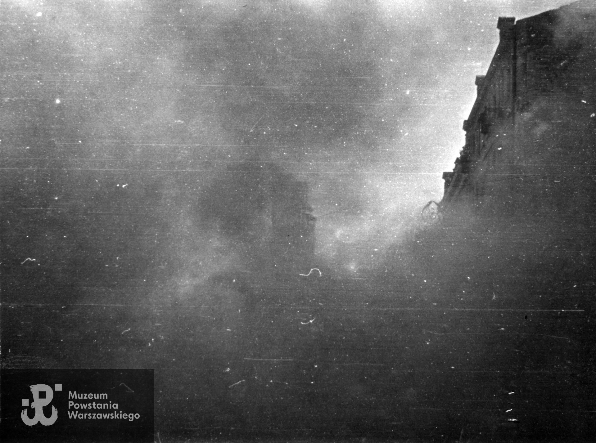 Fotografia autorstwa Zbigniewa Grochowskiego wykonana podczas Powstania Warszawskiego, przedstawiająca dom w kłębach dymu. Fot. ze zbiorów Muzeum Powstania Warszawskiego, sygn. MPW-IP/2710 (MPW-GI-4000/15/06)