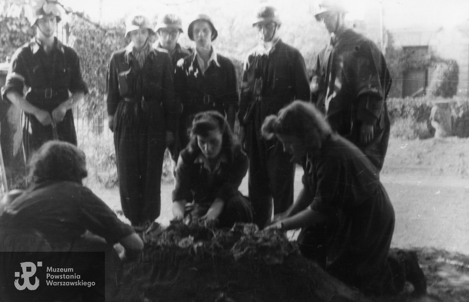 Fotografia z Powstania Warszawskiego. Śródmieście Południowe, pl. Trzech Krzyży. Mogiła strz. Witolda Hermanowskiego "Świta" z I plut. "Kłosa" 3 komp. "Redy" Batalionu "Miłosz" na terenie Instytutu Głuchoniemych i Ociemniałych przy pl. Trzech Krzyży 4/6. Na pierwszym planie od lewej: Helena Schabińska - Modrzejewska "Dzidka", Hanna Baranowska "Lalka", Wacława Sutowska "Aćka". Na drugim planie pierwszy z lewej - kpr. pchor. Juliusz Sylwin Pietrzykowski "Teddy", pierwszy z prawej - kpr. pchor. Stanisław Szabłowski "Witeź". Autorem zdjęcia jest Wojciech Marczyński "Bogusław". Fot. ze zbiorów Muzeum Powstania Warszawskiego, sygn. MPW-IP/7983
