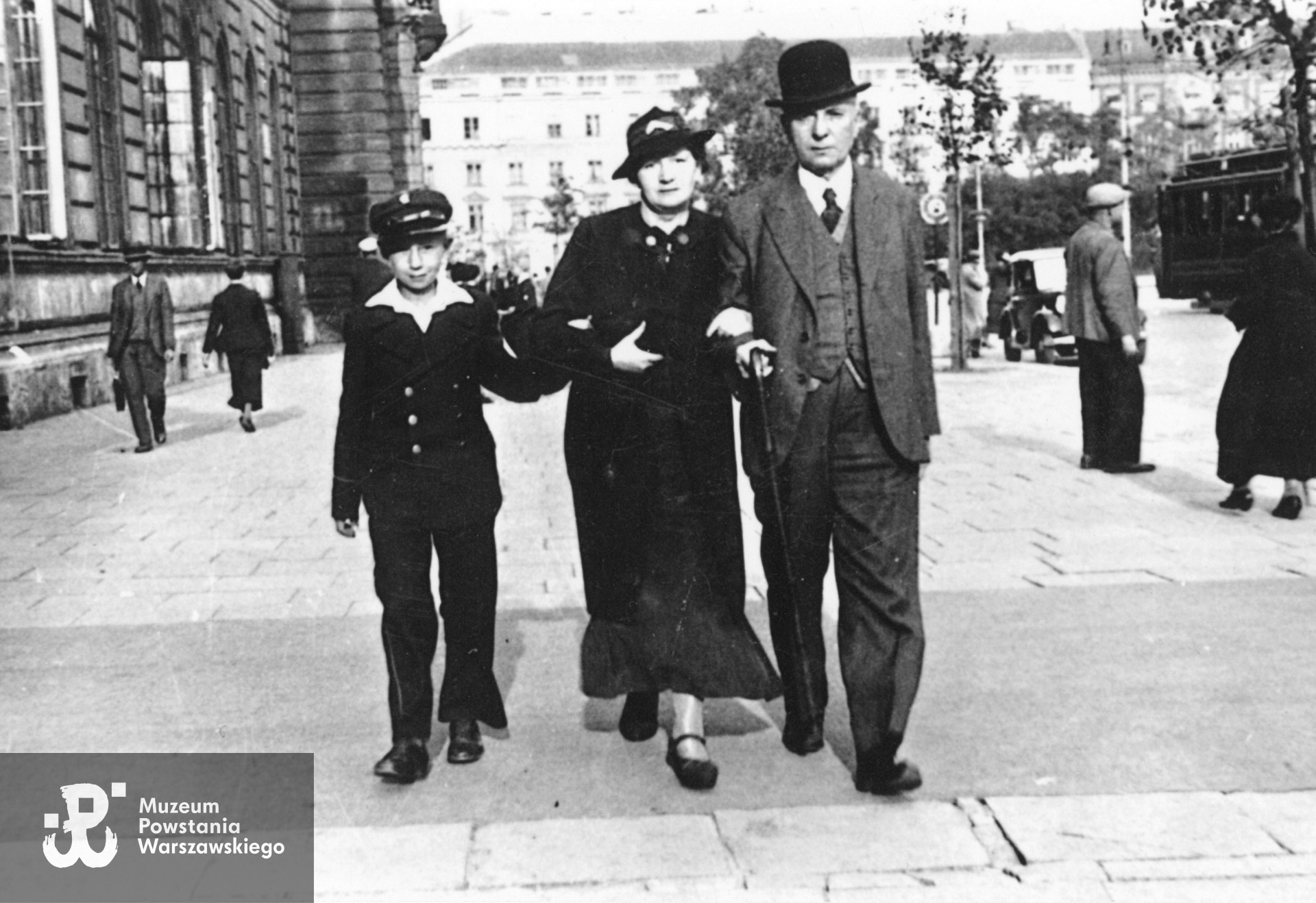  Fotografia przedwojenna, wykonana ok. 1936 r. przedstawiająca Henryka z rodzicami Wacławem i Jadwigą na Placu Teatralnym w Warszawie. Po lewej widoczny Pałac Jabłonowskich (Ratusz), w tle zabudowania ulicy Focha (obecnie ul. Moliera) - kamienica T. A. Uruskiego przy ul. Focha 12 róg Senatorska 19 (zniszczona w 1944 r.). Fot. ze zbiorów rodzinnych, odbitkę nadesłała p. Elżbieta Janik.