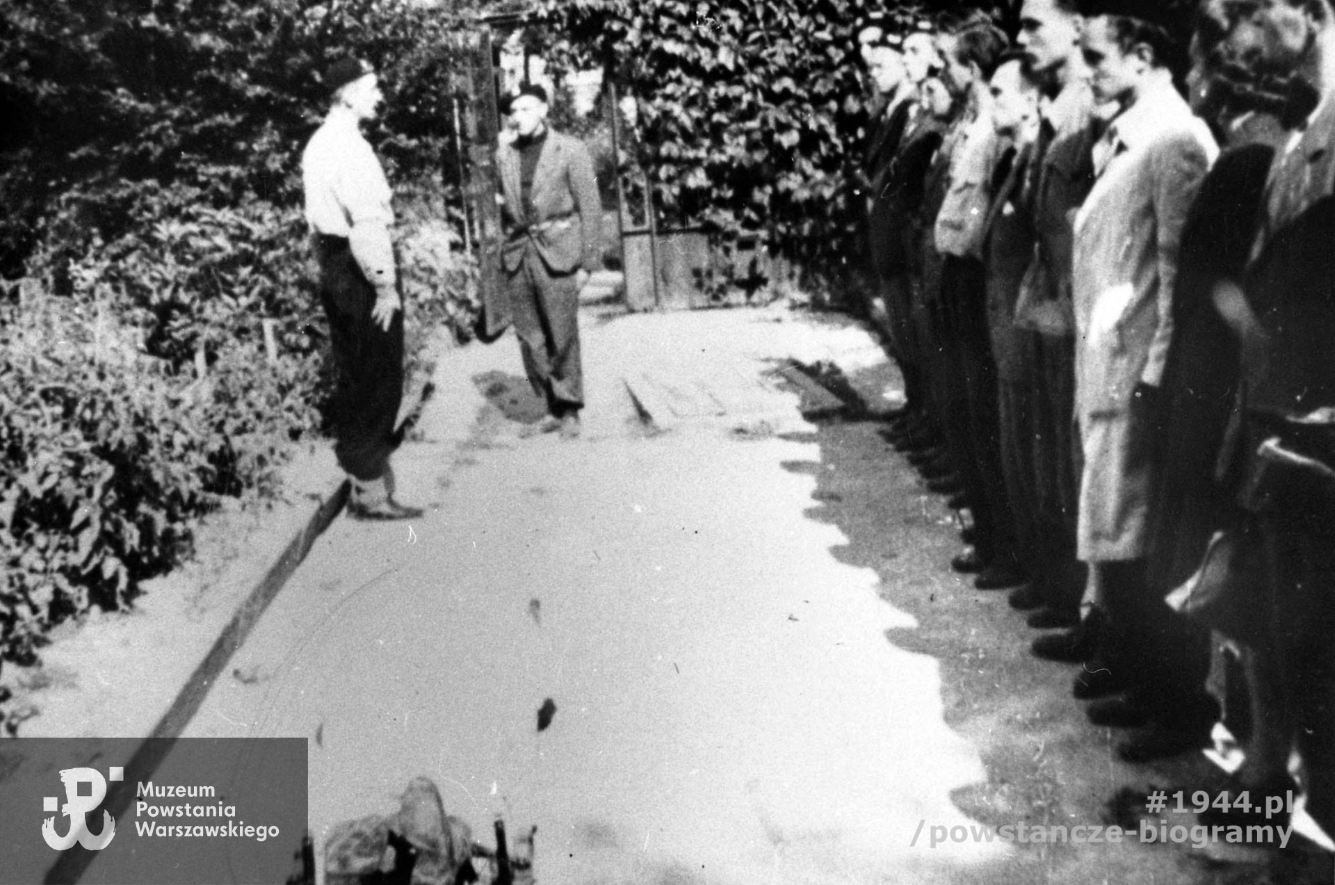 Zdjęcie filmowe z Powstania Warszawskiego. Mokotów, ulica Puławska 134 róg Naruszewicza. Pogrzeb ppor. Stanisława Jenike "Hański", zastępcy dowódcy plutonu 1110 dywizjonu "Jeleń". Stoją od lewej: rtm. Lech Głuchowski "Jeżycki" dowódca dywizjonu, por. Konstanty Bronikowski "Kostecki", wachm. pchor. Henryk Sobański "Sułkowski", st. ułan pchor. Tadeusz Doberski "Dobnia", st. ułan pchor. Ludwik Dunin "Włast", plut. Balon "Cepeliński", NN, wachm. st. ułan pchor. Jerzy Tyrawski "Tomaszewski", st. ułan pchor. Ryszard Pestkowski "Olchowicz", st. ułan pchor. Włodzimierz Drecki "Kawka", st. ułan pchor. Zbigniew Hellon "Kumpel", sanit. Alina Ciembroniewicz-Zabiełło "Alina". Ze zbiorów Muzeum Powstania Warszawskiego, sygn. MPW-IH/1212