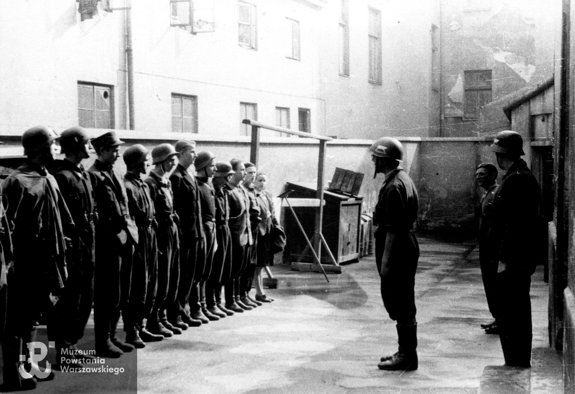 Fotografia z Powstania Warszawskiego. Śródmieście Południowe, ul. Książęca. Zbiórka drużyny wypadowej 1. plutonu "Kłosa" 3. kompanii "Redy" batalionu "Miłosz" na podwórzu kamienicy przy ul. Książęcej 23. Od lewej: kpr. pchor. Stanisław Szabłowski "Witeź", sierż. pchor. Juliusz Pietrzykowski "Teddy", łączn. Leszek Piotrowski "Tygrys", strz. Witold Hermanowski "Świt", strz. Jerzy Ryszard Rosiak "Pantera", st. strz. Ryszard Zieliński (?) "Desant", strz. Stanisław Białowąs "Jajko", NN, NN, NN, strz. Zofia Tomasik "Teresa". Przed frontem ppor. Henryk Bigajski "Potocki", NN i por. Marian Stasiak "Czółno". Fot. ze zbiorów Muzeum Powstania Warszawskiego, sygn. MPW-IS/820 (P/8598/16).