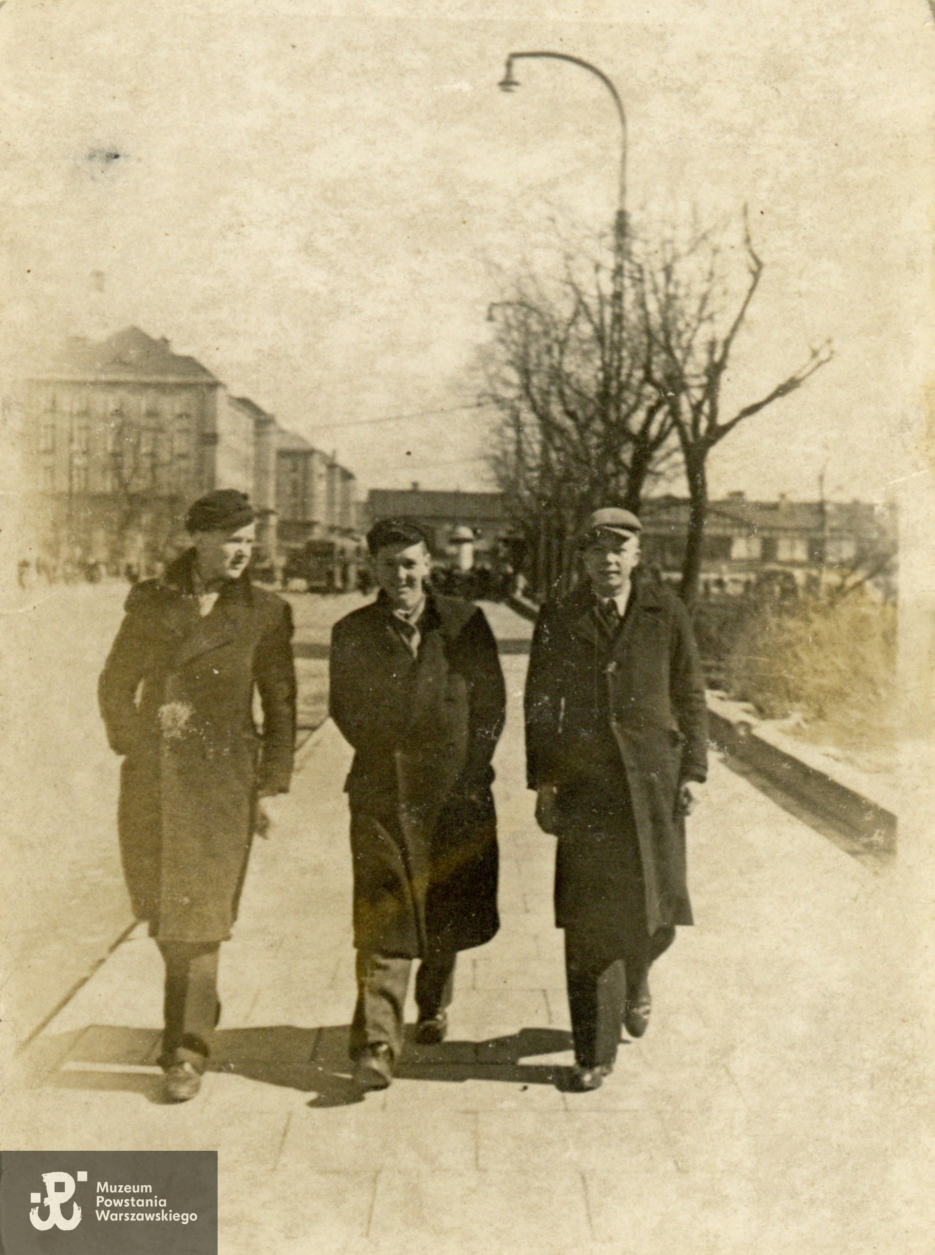 Fotografia z okresu okupacji niemieckiej, Adolf Pursa "Grajdołek" (idący w środku) wraz z kolegami. Praga,  skrzyżowanie ulic Targowej i Wileńskiej, w tle widoczny modernistyczny budynek Dyrekcji Okręgowej Kolei Państwowych  przy ul. Targowej 74, projektu Mariana Lalewicza (z lewej) oraz parterowy budynek Dworca Wileńskiego (po prawej). Fot. ze zbiorów rodzinnych, do wykonania kopii udostępniła p. Elżbieta Wysocka, córka Powstańca. Skany wykonano w Muzeum Powstania Warszawskiego w grudniu 2023 r. 