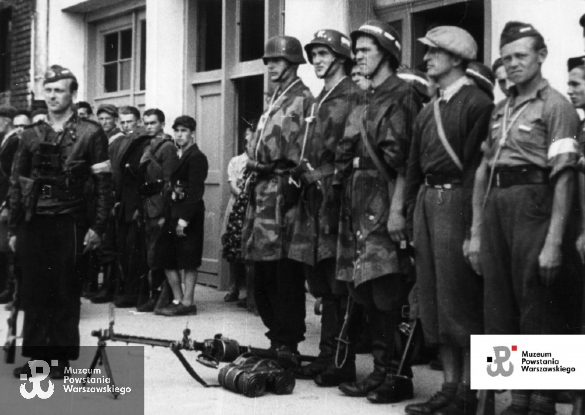 Zdjęcie filmowe z Powstania Warszawskiego. Mokotów, ulica Puławska 132. Przegląd oddziałów przybyłych z Lasów Chojnowskich. Kompania "Krawiec". Przed kompanią w furażerce dowódca por. Stanisław Milczyński "Gryf". W pierwszym szeregu stoją od lewej: strz. Bolesław Wiewióra "Samson", strz. Józef Wilczak "Wilk", kpr. Stanisław Sekuła "Śmiały", w czapce cyklistówce kpr. pchor. Tadeusz Kozłowski "Kozak", kpr. Władysław Zygański "Żuk". W rzędzie w głębi od prawej: NN, strz. Kazimierz Wilczak "Spokojny", strz. Józef Pyrka "Grot", st. strz. Marian Staczkun "Mirek". Ze zbiorów Muzeum Powstania Warszawskiego, sygn. MPW-IK/1677