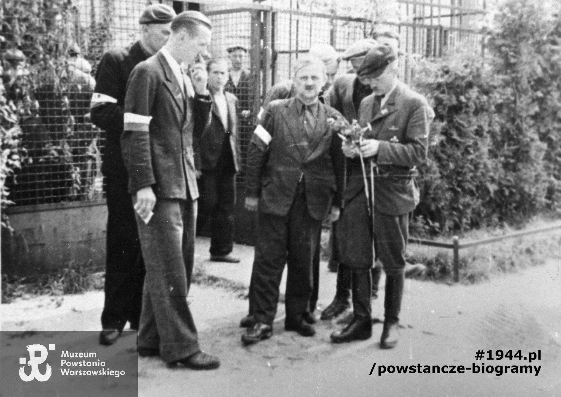 Fotografia z Powstania Warszawskiego. Żoliborz, żołnierze Zgrupowania "Żaglowiec" w towarzystwie dowódcy "Żywiciela" po nabożeństwie przy ul. Pogonowskiego 22. Od lewej: ppor. Stefan Szuba "Leszcz" - zastępca dowódcy Zgrupowania, ppor. Zenon Czarnomski "Krzew" adiutant "Żaglowca", w środku ppłk. Mieczysław Niedzielski "Żywiciel" - dowódca II Obwodu, kpt. Marian Kamiński "Żaglowiec" "Jur" - dowódca Zgrupowania "Żaglowiec", trzyma w ręku wiązankę kwiatów. Fot. ze zbiorów Muzeum Powstania Warszawskiego, sygn.  MPW-IP/5436