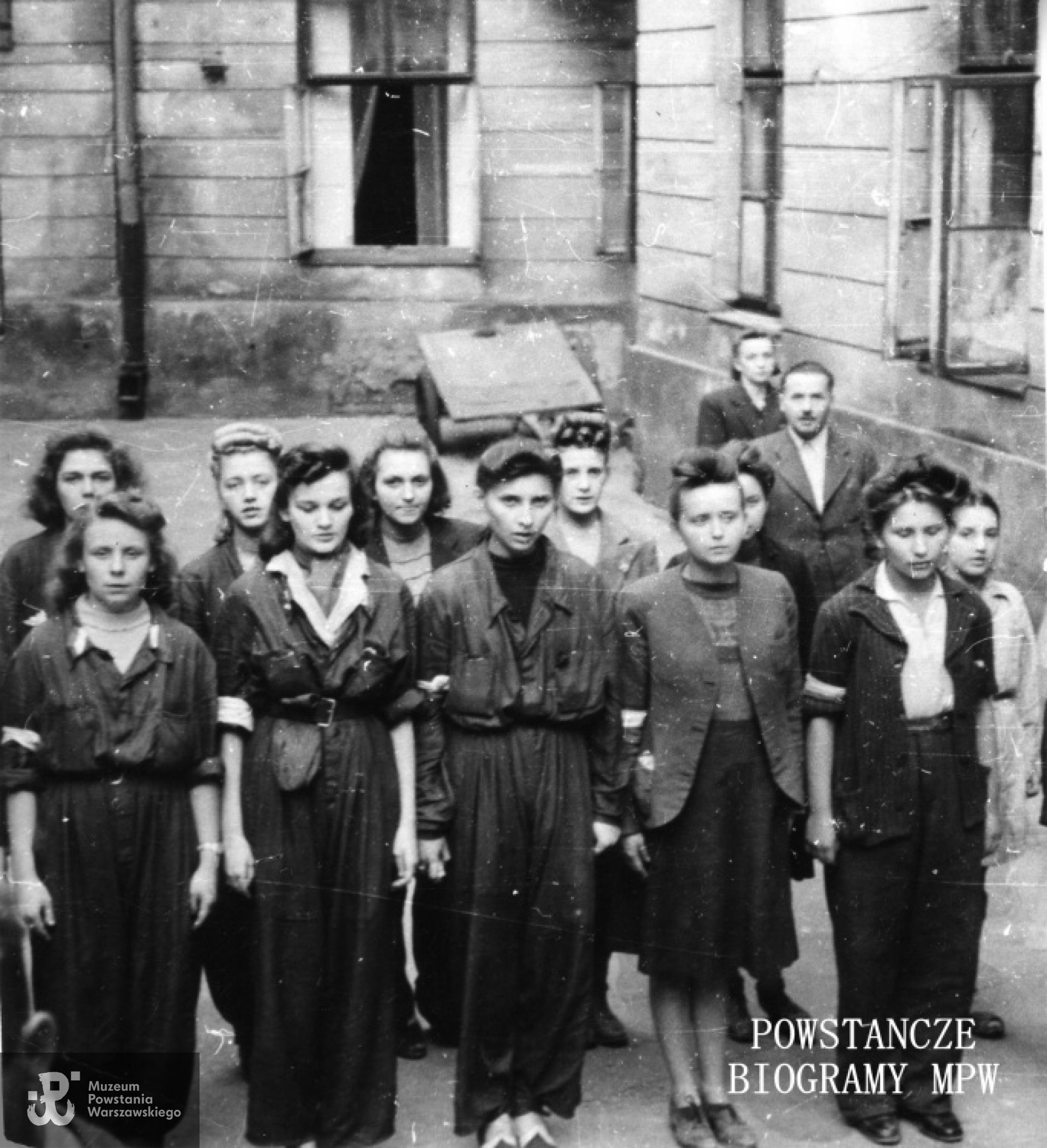 Fotografia z Powstania Warszawskiego. Śródmieście Południowe. Sanitariuszki z 1. plutonu "Kłosa" 3. kompanii "Redy" batalionu "Miłosz" podczas mszy na podwórzu kamienicy. Hanna Baranowska "Lalka" stoi w pierwszym rzędzie druga od lewej. Kadr większego ujęcia. Autorem zdjęcia jest Wojciech Marczyński "Bogusław".  Fot. ze zbiorów Muzeum Powstania Warszawskiego, sygn. MPW-IK/2714