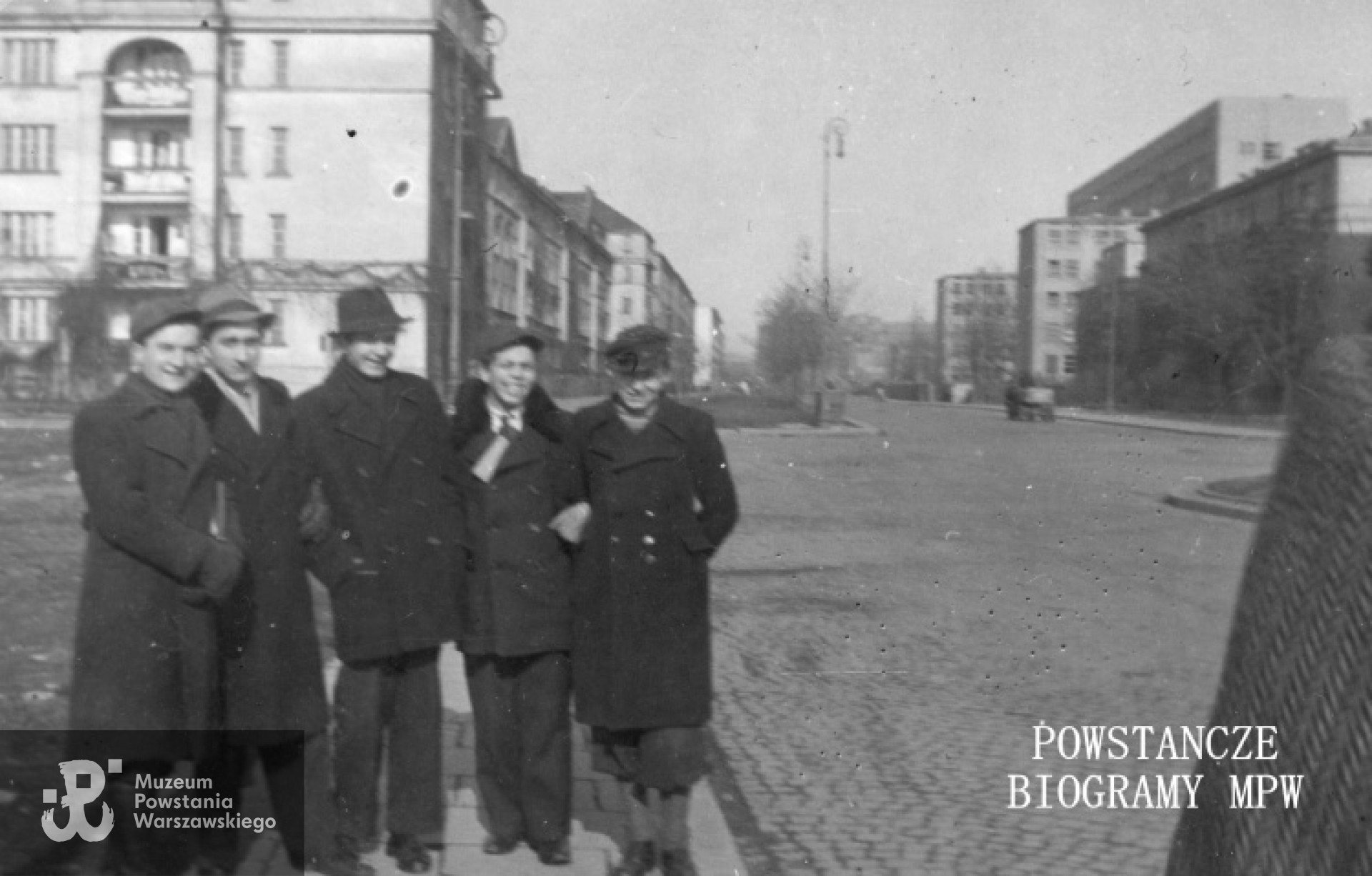 Aleja Niepodległości przy skrzyżowaniu z ul. Wawelską Ulica. Ujęcie w kierunku północnym, po lewej kamienica al. Niepodległości 217, po prawej dom al. Niepodległości 212, dalej w tle widoczny gmach 1. Szpitala Okręgowego im. Marszałka Józefa Piłsudskiego - al. Niepodległości 218, róg 6 Sierpnia. Stoją od lewej: Aleksander Kamiński, Leszek Kołodziejczyk, Tadeusz Blejarski, Lech Kułak, Stefan Bilski. MPW-IP/5248
