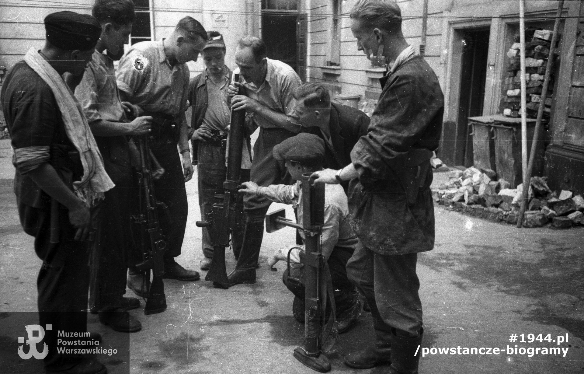 Plut. pchor. Adam Podkóliński "Michał", "Olszewski" (trzeci od lewej) prezentuje grupie powstańców z kompanii "Janusza" z batalionu "Harnaś" niemiecki lekki karabin maszynowy (leMG 08/15) zdobyty po ataku na Komendę Policji. Powstaniec na pierwszym planie po prawej trzyma brytyjski granatnik przeciwpancerny PIAT. Fot. ze zbiorów Muzeum Powstania Warszawskiego, sygn. MPW-IN/10205. Autorem zdjęcia jest Joachim Joachimczyk "Joachim"