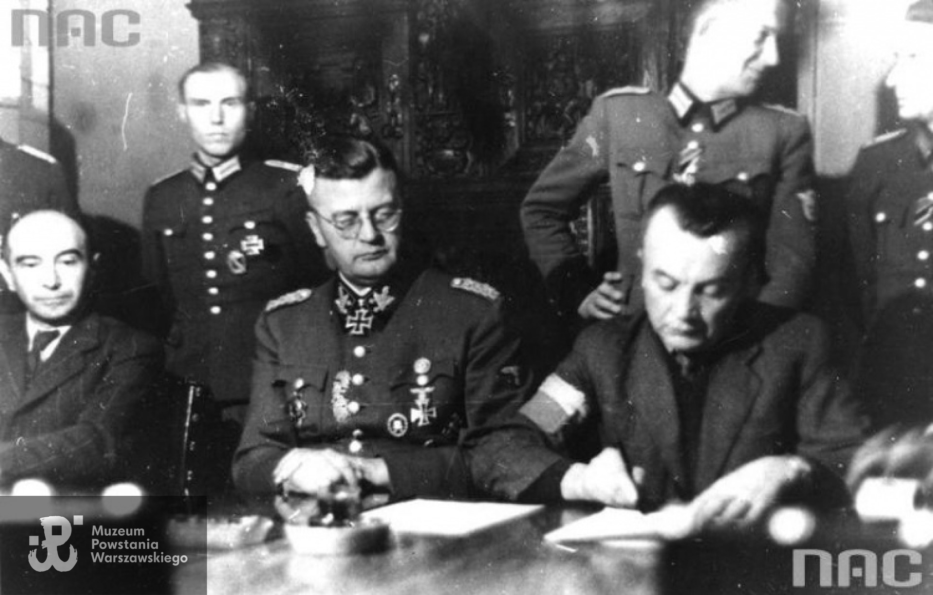 Ożarów, Dworek Reicherów, październik 1944 r.  Akt podpisywania dokumentów o zawieszeniu broni i przyznaniu Powstańcom Warszawy  praw kombatanckich. Na zdjęciu od lewej pułkownik Iranek Osmecki, niemiecki generał E. von dem Bach, pułkownik Zygmunt Dobrowolski. Fot. ze zbiorów NAC  [www.nac.gov.pl]