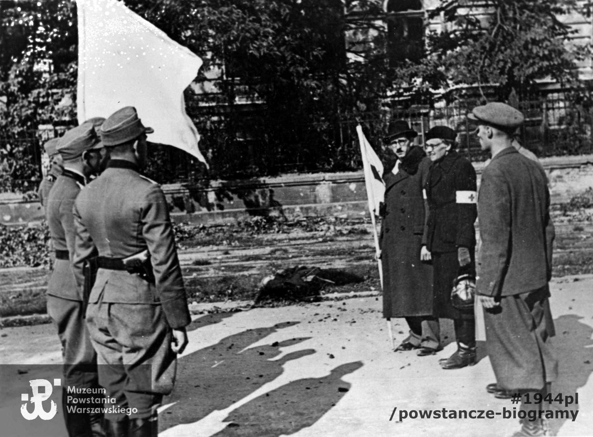 Fotografia z Powstania Warszawskiego. Śródmieście Południowe. Parlamentariusze polscy na ulicy 6 Sierpnia (obecnie Nowowiejska) i delegacja niemiecka przed pertraktacjami w sprawie kapitulacji Powstania. W tle gmach Politechniki Warszawskiej. Po prawej stronie przedstawiciele Polskiego Czerwonego Krzyża - Maria hrabina Tarnowska i dr Hieronim Bartoszewski (w okularach i czarnym kapeluszu). Fot. ze zbiorów Muzeum Powstania Warszawskiego, sygn. MPW-IH/4297