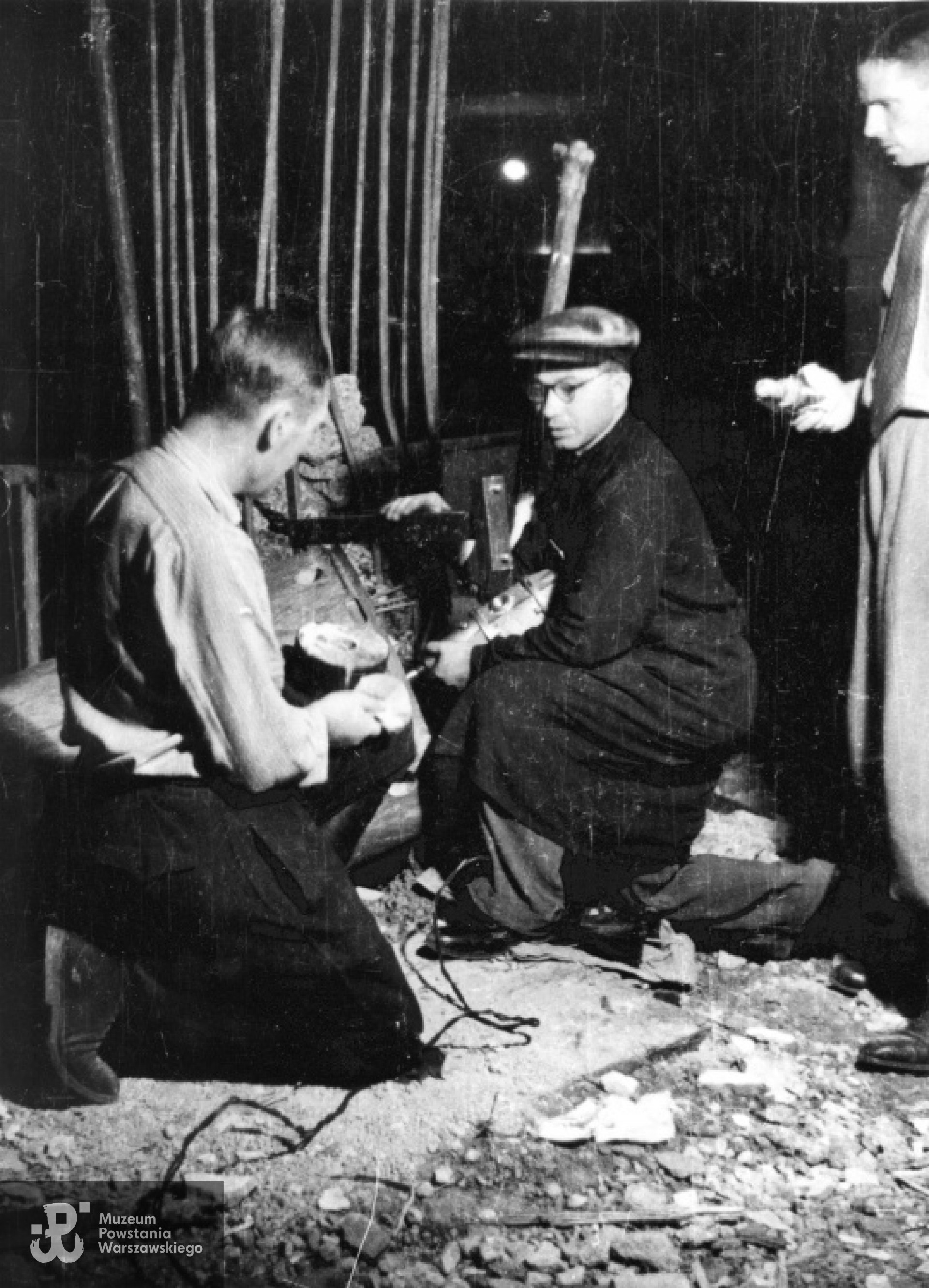 Rozbrajający niewybuch pocisku w restauracji "Adria" przy ulicy Moniuszki 10; od lewej: st. sierż. Józef Gorzkowski "Szczepcio", st. sierż. Tadeusz Fabianowski "Fabian", ppor. Stanisław Dutkiewicz "Pillert". Fotografia  autorstwa Eugeniusza Lokajskiego „Broka”, zbiory Fototeki  MPW, sygn.  MPW-IN/378.  Prawa autorskie: MPW