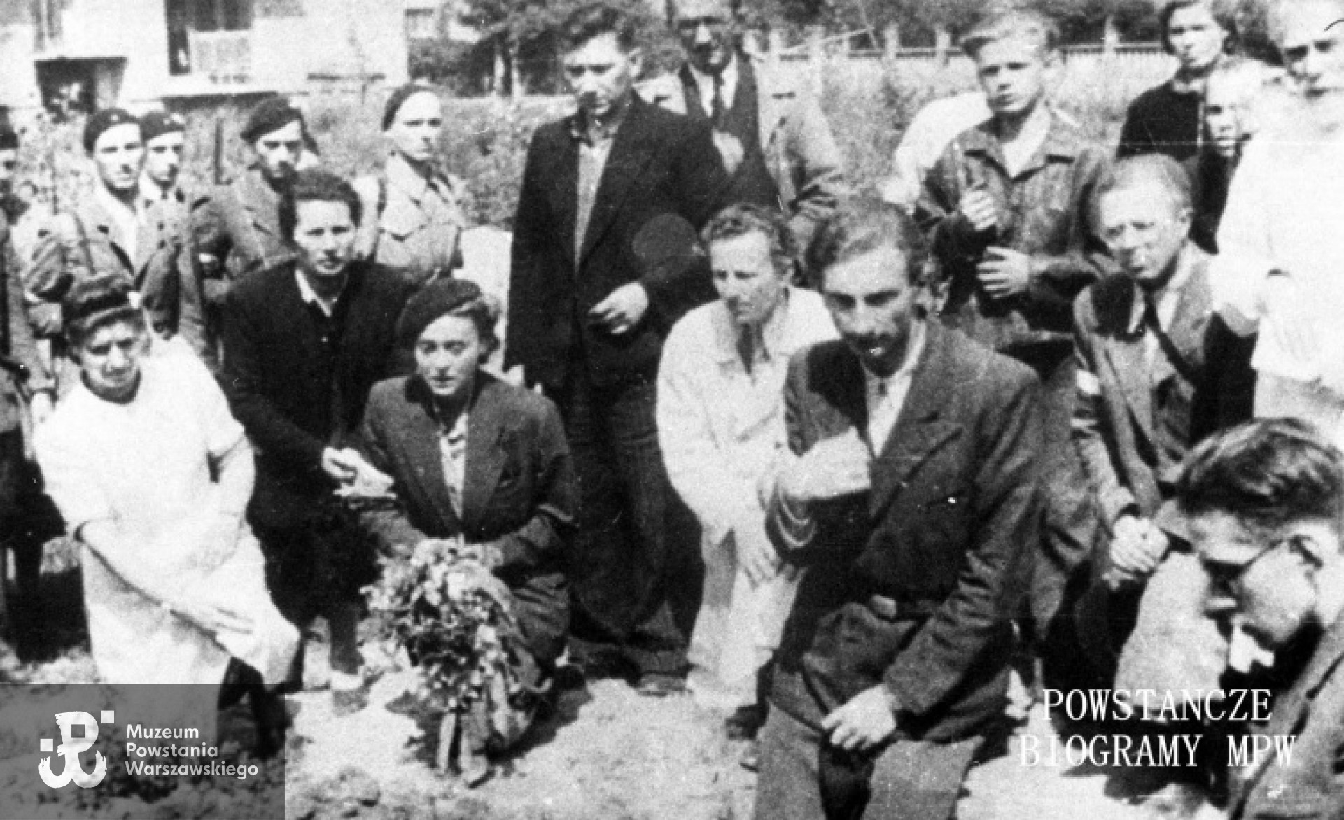 Zdjęcie filmowe z Powstania Warszawskiego. Mokotów, cmentarz powstańczy przy Szpitalu Elżbietanek w rogu ulic Goszczyńskiego i Tynieckiej. Grupa powstańców na pogrzebie sanitariuszki Anny Habrowskiej "Marii" z plutonu 1110 dywizjonu "Jeleń". Na pierwszym planie kpr. pchor. Andrzej Bontemps "Mnich". Z kwiatami sanitariuszka Alina Ciembroziewicz-Zabiełło "Alina". Od prawej profilem st. ułan pchor. Andrzej Czernik "Cebion", w okularach st. ułan pchor. Tadeusz Doberski "Dobnia". Z tyłu trzeci od lewej st. strz. pchor. Józef Ruszczyński "Lis", piąty st. ułan pchor. Włodzimierz Drecki "Kawka". Fot. ze zbiorów Muzeum Powstania Warszawskiego, sygn. MPW-IH/1225