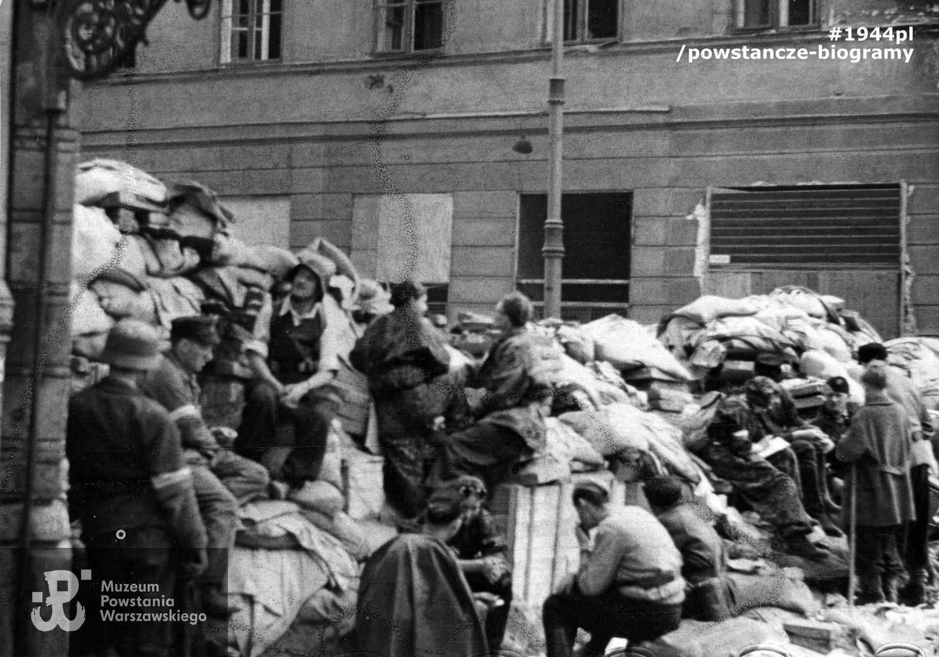 Fotografia z Powstania Warszawskiego Starówka. Powstańcy na barykadzie "Żyrardów", zwanej też redutą "św. Trójcy", przegradzającej ul. Bielańską na wysokości wylotu ul. Daniłowiczowskiej. W tle widoczny fragment elewacji dawnego Hotelu Lipskiego przy ul. Bielańskiej 3. Autorem zdjęcia jest Józef Jerzy Karpiński. Fot. ze zbiorów Muzeum Powstania Warszawskiego, sygn. MPW-IK/1433