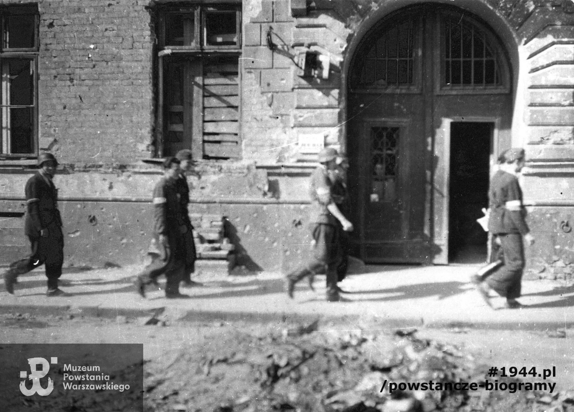 Fotografia z Powstania Warszawskiego. Wymarsz plutonu "Rygla" zgrupowania "Bartkiewicz" na akcję w Ogrodzie Saskim ulicą w rejonie Jasnej - Rysiej - Szkolnej. Dwójkami idą od lewej: NN i NN, st. strz. Zbigniew Kurbiel "Krakus" (z zewnętrznej) i kpr. pchor. Andrzej Starwiński "Chimera", kpr. pchor. Andrzej Gliński "Leszczyc" i strz. Władysław Maydell "Waldemar", kpr. z cenz. Jerzy Jenike "Zwierz" i kpr. pchor. Janusz Sawicki "Zabawa". Ze zbiorów Muzeum Powstania Warszawskiego, sygn. MPW-IP/3848