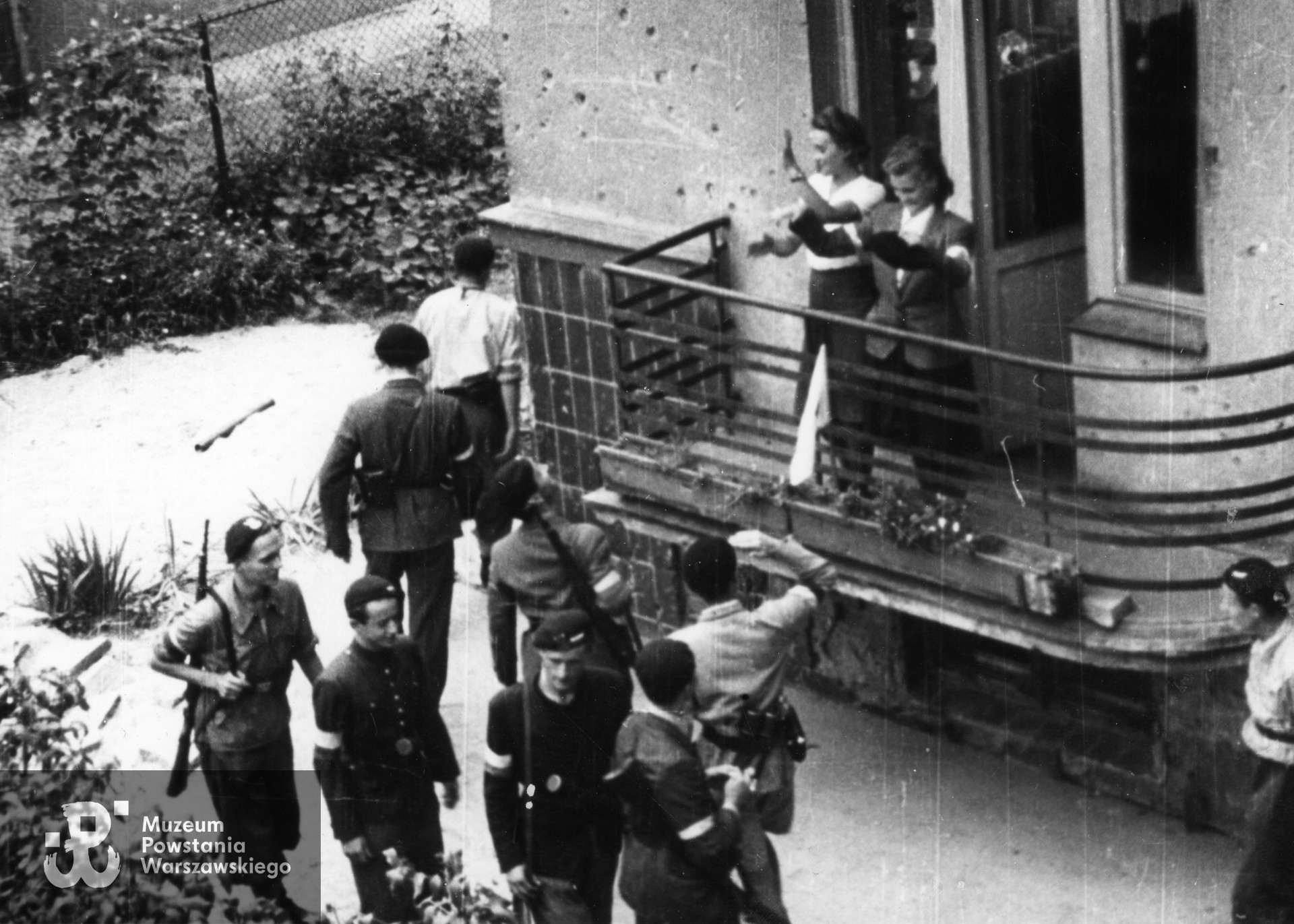 Zdjęcie filmowe z Powstania Warszawskiego: Mokotów, podwórko domu przy ulicy Odyńca 7 róg Tynieckiej. Grupa powstańców z plutonu 1110 dywizjonu "Jeleń" wyrusza na patrol. Żegnają ich stojące na balkonie pierwszego piętra sanitariuszki, od lewej sanit. Maria Kosicka "Małgorzata" i sanit. Alina Ciembroniewicz-Zabiełło "Alina". W szeregu od lewej st. ułan pchor. Włodzimierz Drecki "Kawka" z, NN, st. ułan pchor. Władysław Grabiński "Pilawa" (z karabinem), pozostali NN. Autor Roman Banach "Świerk”. Ze zbiorów Muzeum Powstania Warszawskiego, sygn. MPW-IK/1699