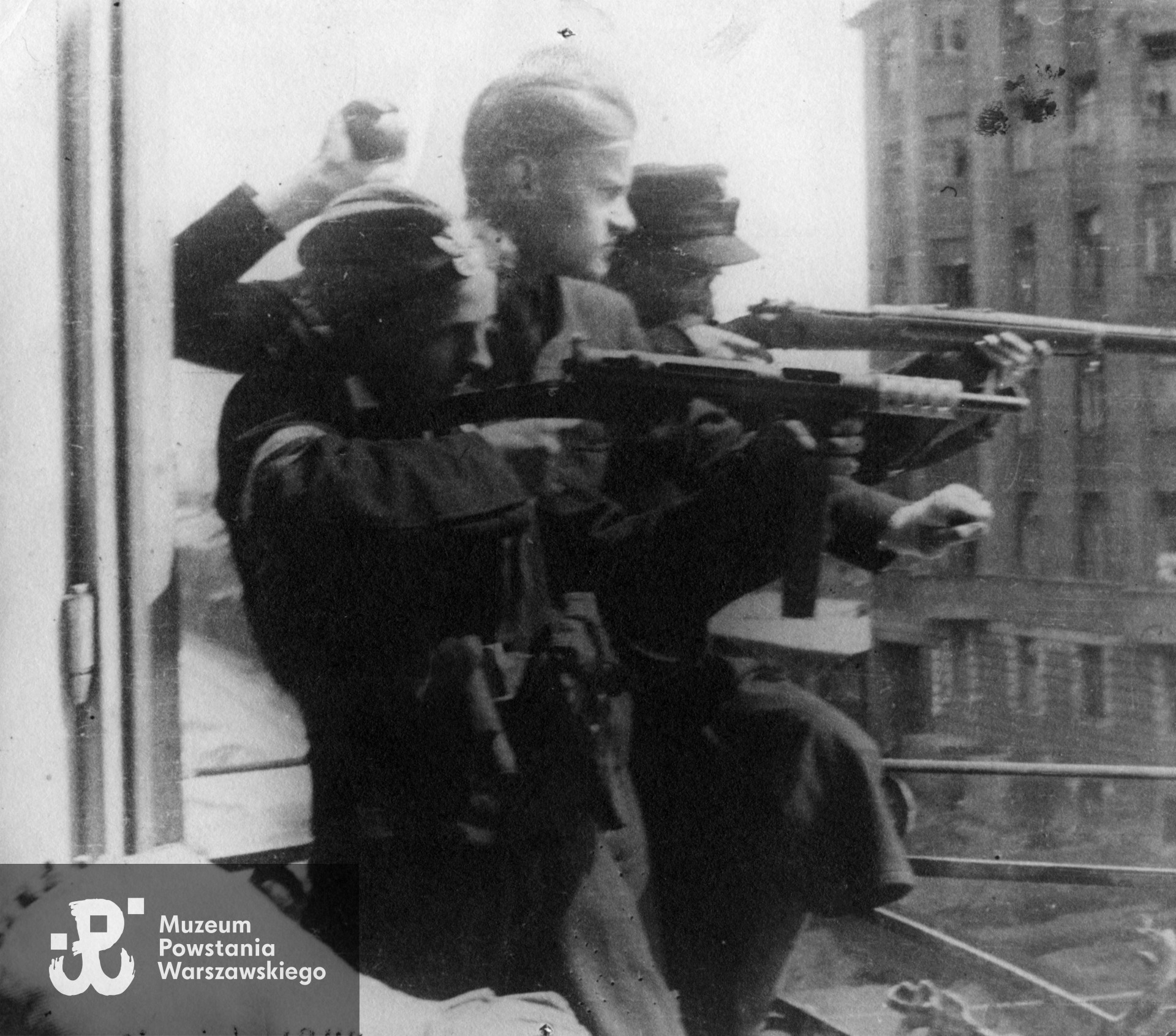 Fotografia z Powstania Warszawskiego. Śródmieście Północne. Powstańcy z 3 kompanii, I batalionu "Lech Żelazny" zgrupowania "Chrobry II" na balkonie kamienicy przy ul. Chmielnej 126, róg Żelaznej 25. ujęcie w kierunku wschodnim. Od lewej: Gerard Niewiadomski "Pozorny" (trzyma pistolet maszynowy "Błyskawica"), Zygmunt Krzywicki 'Wiktor", "Pantera".  W tle po prawej fragment Domu Kolejowego przy ul. Chmielnej 73b. Fot. ze zbiorów Muzeum Powstania Warszawskiego, sygn. MPW-IP/6299