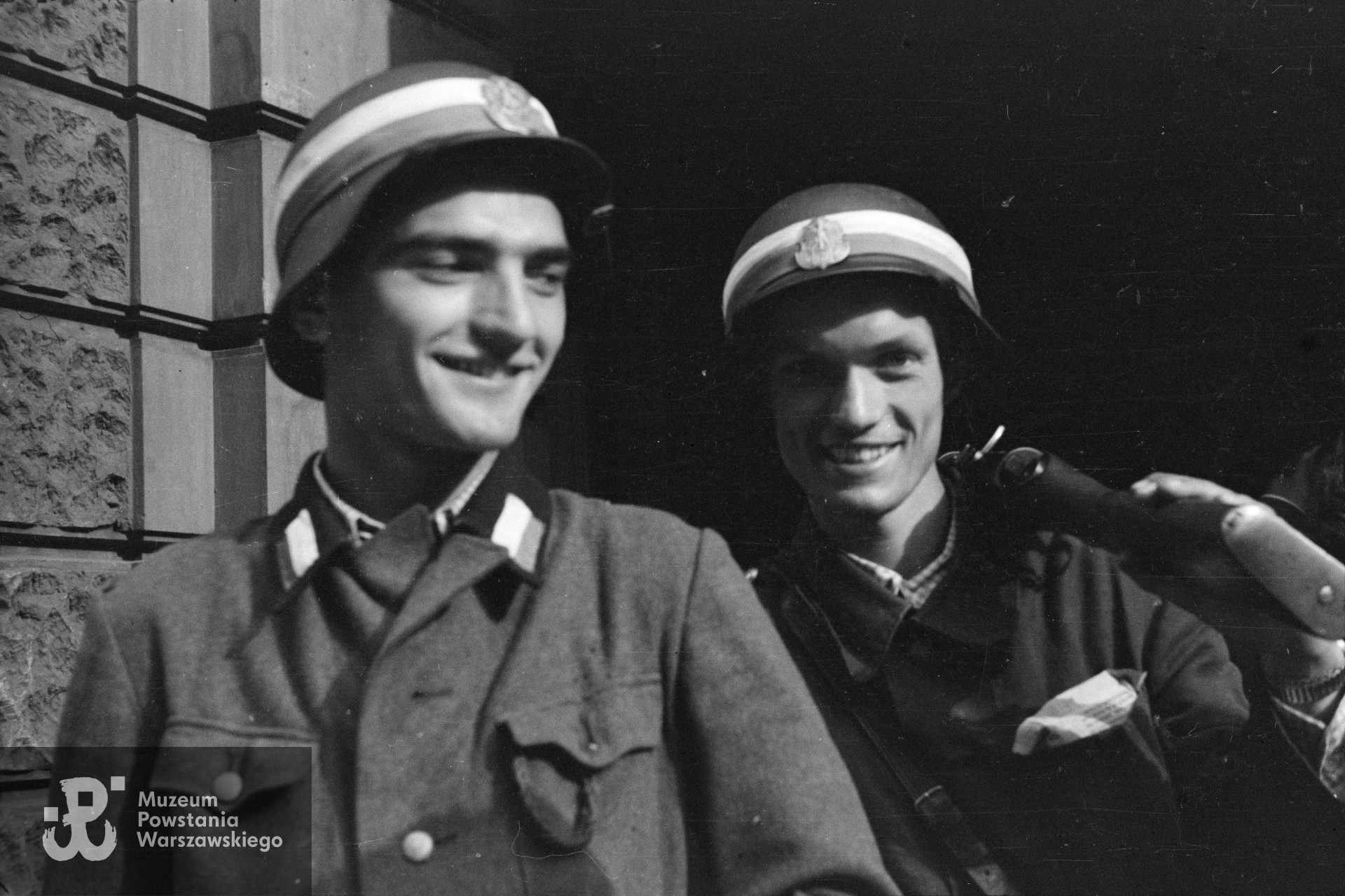Fotografia z Powstania Warszawskiego, I dekada sierpnia 1944 r.  Śródmieście Północne. Plut. pchor. Włodzimierz Radajewski "Rataj" (z lewej) i plut. pchor. Jerzy Tyczyński "Jur" (z prawej) w bramie kamienicy przy ulicy Moniuszki 11. Fot. autorstwa Eugeniusza Lokajskiego ps. "Brok". Ze zbiorów Fototeki MPW, sygn. Fot. autorstwa Eugeniusza Lokajskiego ps. "Brok". Ze zbiorów Muzeum Powstania Warszawskiego, sygn. MPW-IN/196.
