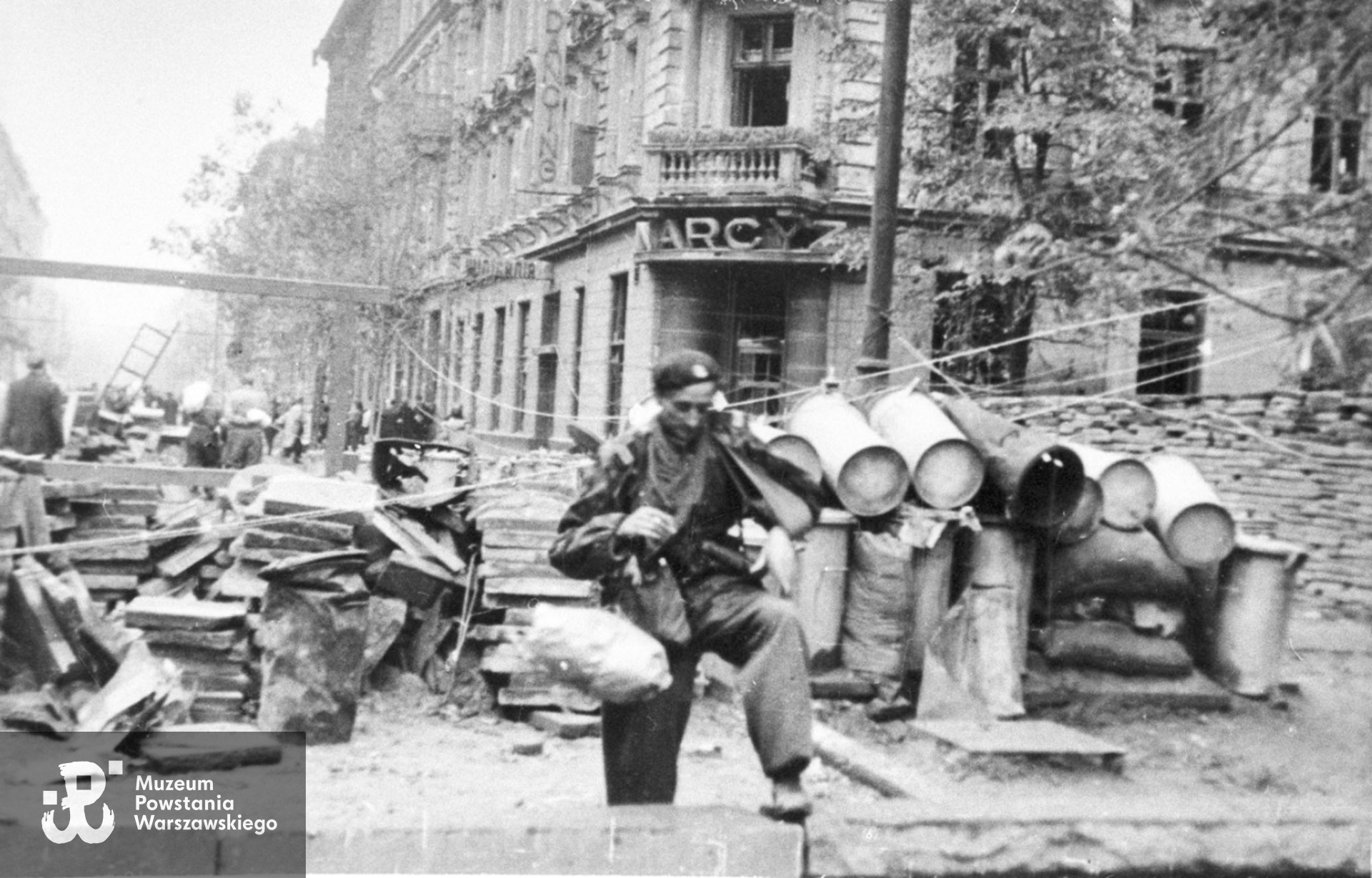Fotografia z Powstania Warszawskiego  autorstwa Bernarda Marwińskiego (PSW). Barykada na skrzyżowaniu ulicy Kruczej i Żurawiej. Ujęcie w kierunku południowym. W tle narożna kamienica Żurawia 19 / Krucza 39 z szyldem restauracji "Narcyz".Fot. ze zbiorów Muzeum Powstania Warszawskiego, sygn. MPW-IH/4411