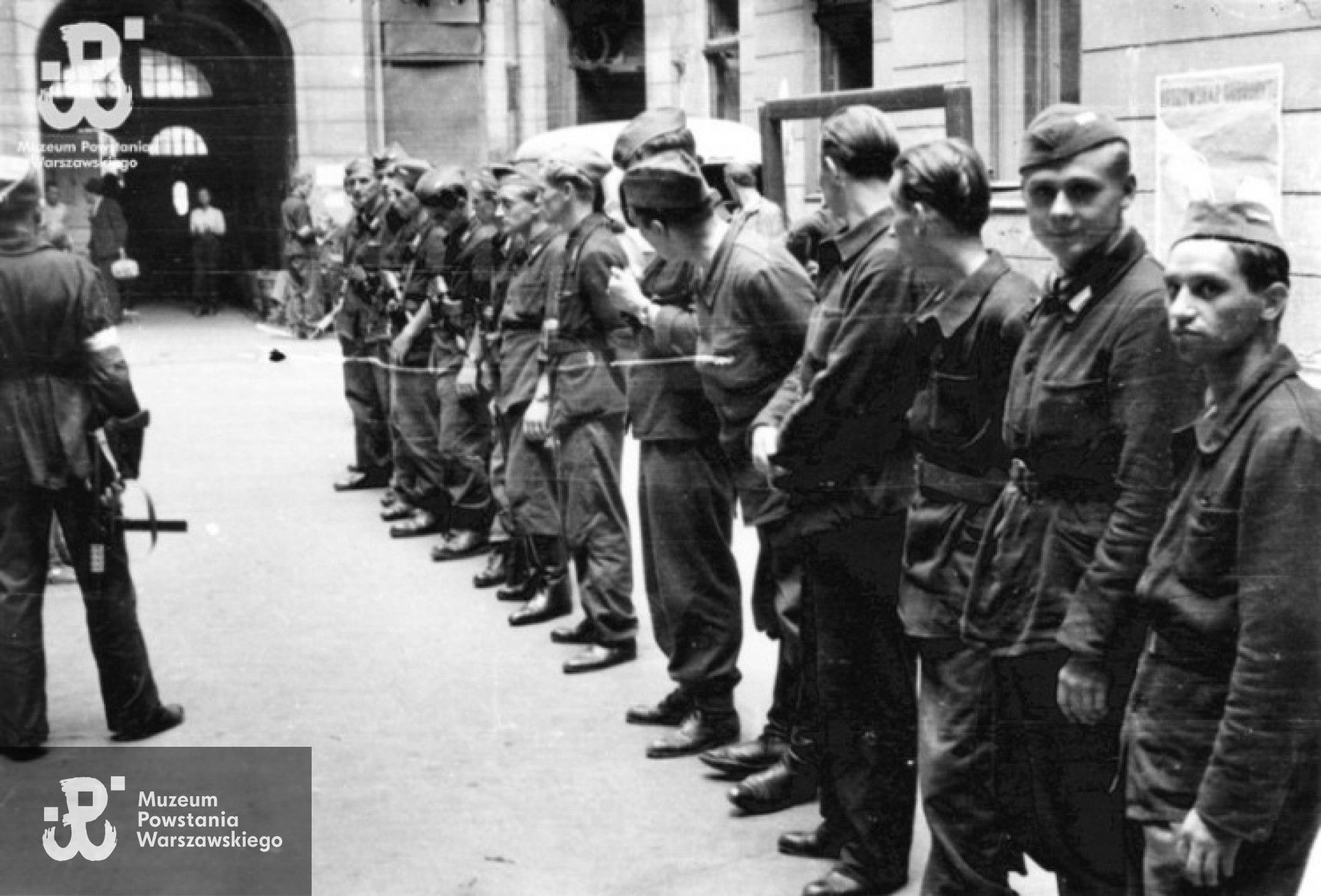 Powstanie Warszawskie, sierpień 1944 r. Zbiórka III plutonu Oddziału Osłonowego WZW na podwórzu kamienicy przy ul. Boduena 2. Od prawej stoją st. strz. Tadeusz Wojda "Rzeźnik", strz. Włodzimierz Leo "Bawół", kpr. pchor. Ryszard Wrzosek "Dick", (NN), kpr. pchor. Tadeusz Bruszewski "Sztubak". Fot. Eugeniusz Lokajski "Brok".