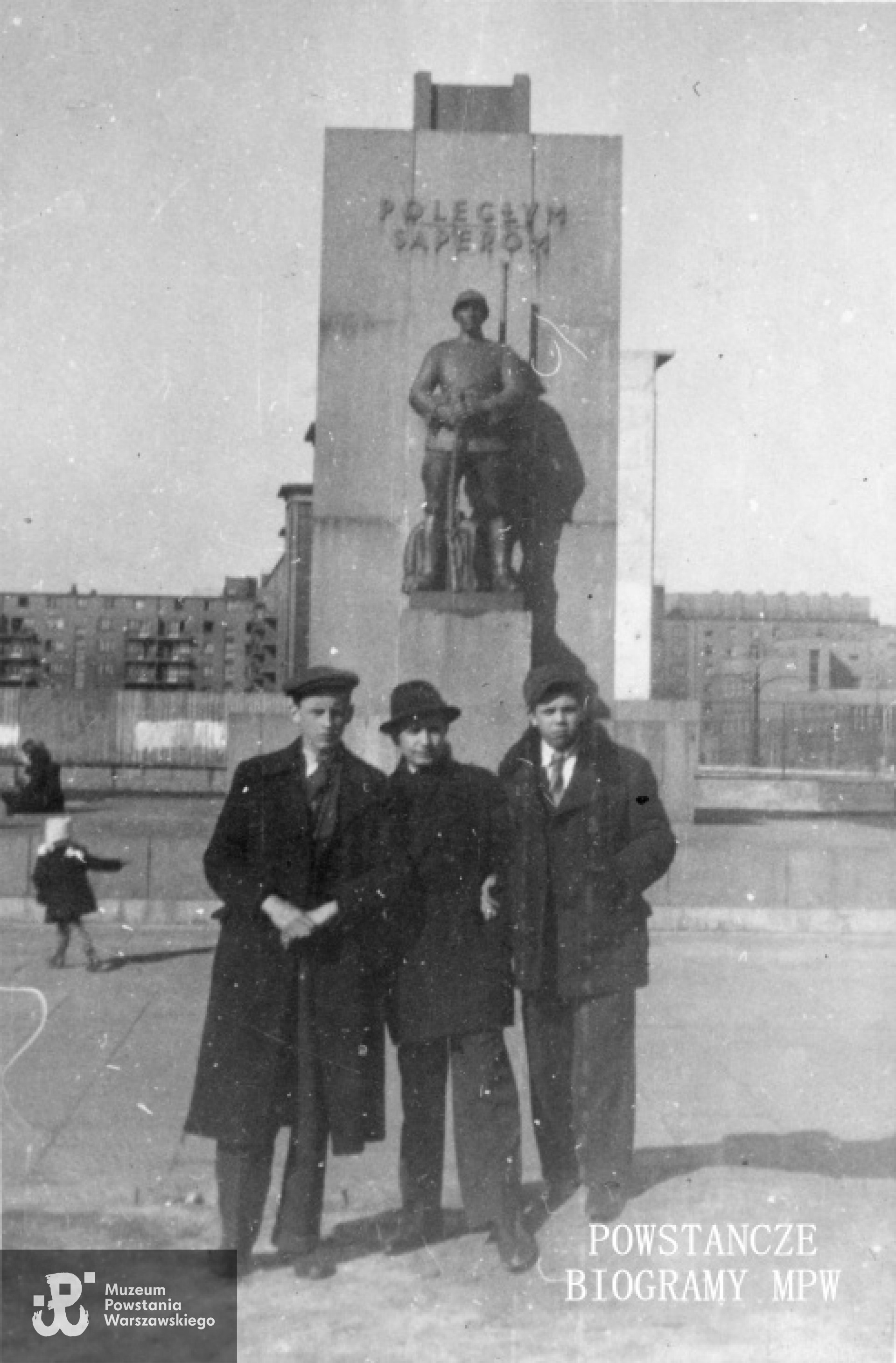 Fotografia z okresu okupacji niemieckiej - 1943 r.  Grupa młodych mężczyzn przed Pomnikiem saperów przy ulicy 6-ego Sierpnia róg alei Niepodlełości Przed Pomnikiem Saperów stoją od lewej: Leszek Szymańczyk, Tadeusz Blejarski, Lech Kułak. MPW-IP/5249
