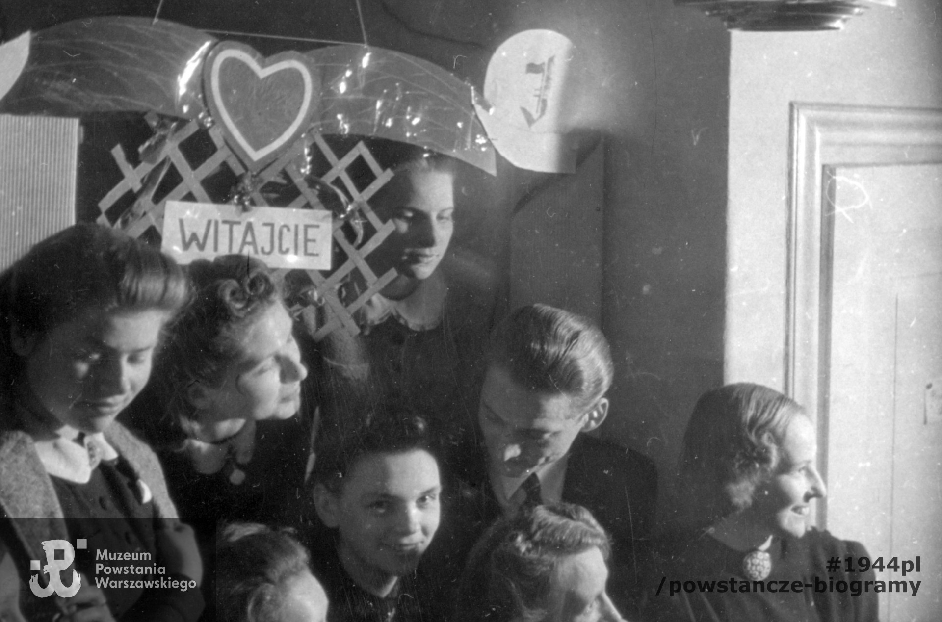 Fotografia z okresu okupacji niemieckiej. Warszawa. Uczestnicy spotkania towarzyskiego (zabawy?) w mieszkaniu rodziny Natansonów przy ul. Tucholskiej 5. Po lewej Alicja i Anna Natanson. Olgierd Budrewicz z pochyloną głową stoi drugi od prawej. Fot. ze zbiorów Muzeum Powstania Warszawskiego, sygn. MPW-IP/6321/69, kolekcja Olgierda Budrewicza