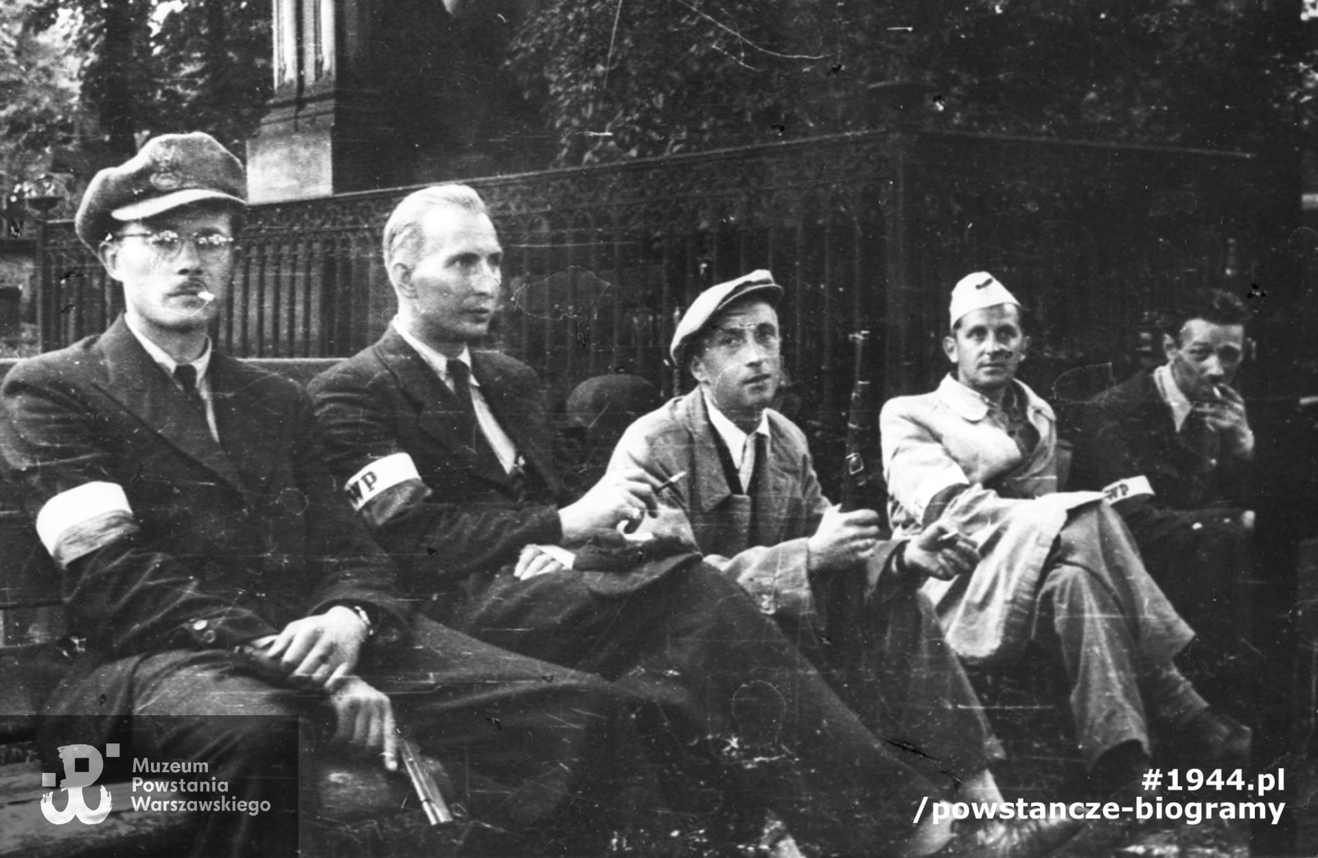 Fotografia z Powstania Warszawskiego. Wola. Godzina „W”. Koncentracja powstańców z plutonu "Agaton" Batalionu „Pięść” na cmentarzu ewangelicko-augsburskim. Pierwszy z lewej siedzi Stefan Bałuk „Kubuś” , obok niego kpr. Seweryn Brwiliński „Adam”, czwarty od lewej Wojciech Bernatowicz. Fot. ze zbiorów Muzeum Powstania Warszawskiego, sygn. MPW-IH/3415.