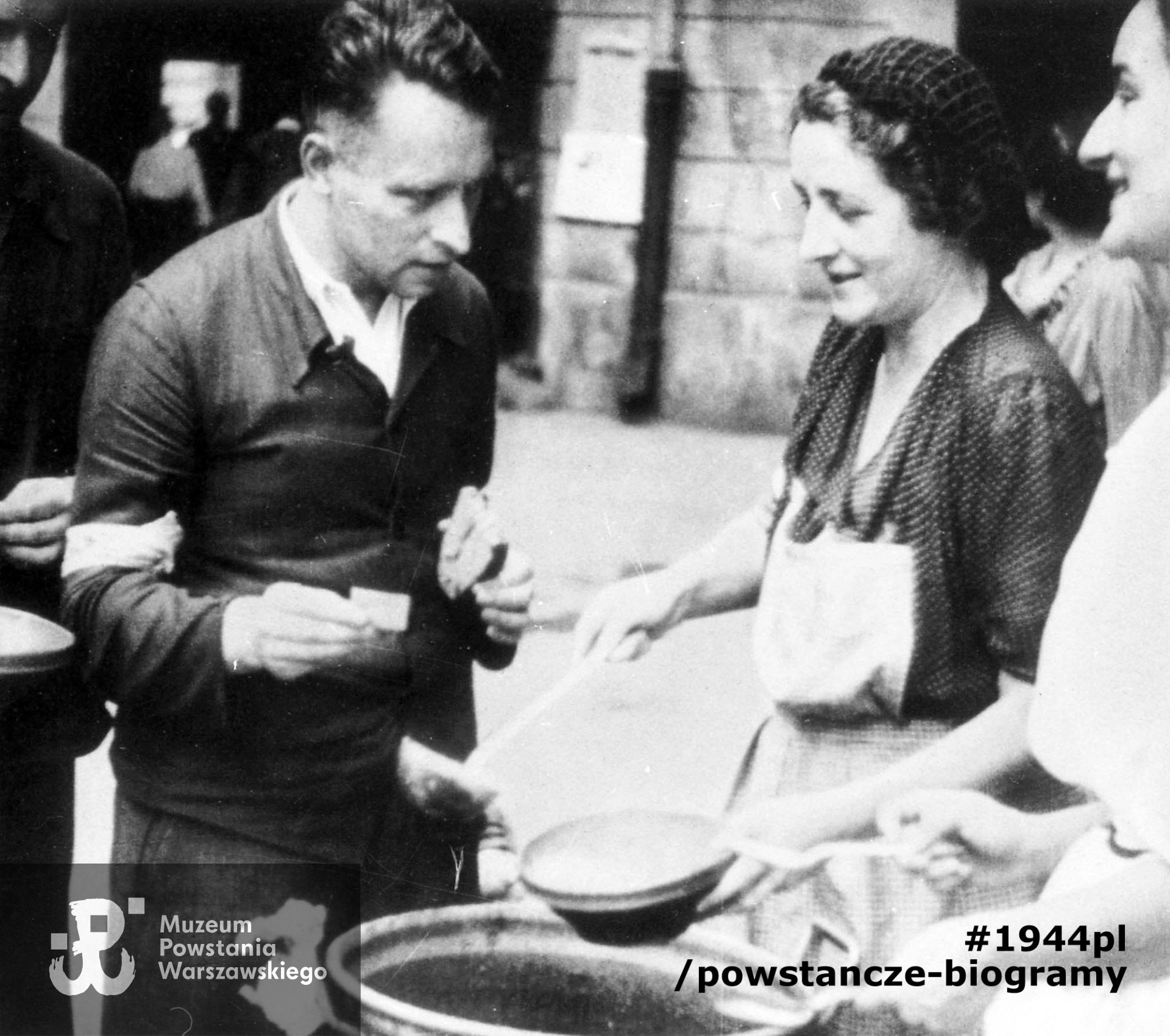 Fotografia filmowa z Powstania Warszawskiego. Śródmieście Północne. Kuchnia żołnierska na podwórzu domu Wedla przy ul. Szpitalnej 8. Członkinie WSK nalewają zupę Tadeuszowi Mikulskiemu "Krasickiemu" z BIP. Ze zbiorów Muzeum Powstania Warszawskiego, sygn. MPW-IH/1499