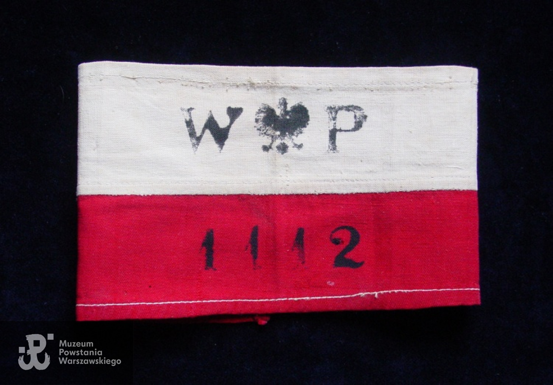 Powstanie Warszawskie. Opaska Krzysztofa Głuchowskiego z plutonu 1112 dywizjonu "Jeleń". Taką opaskę nosił również gen. "Bór" Komorowski i inni oficerowie Komendy Głównej Armii Krajowej