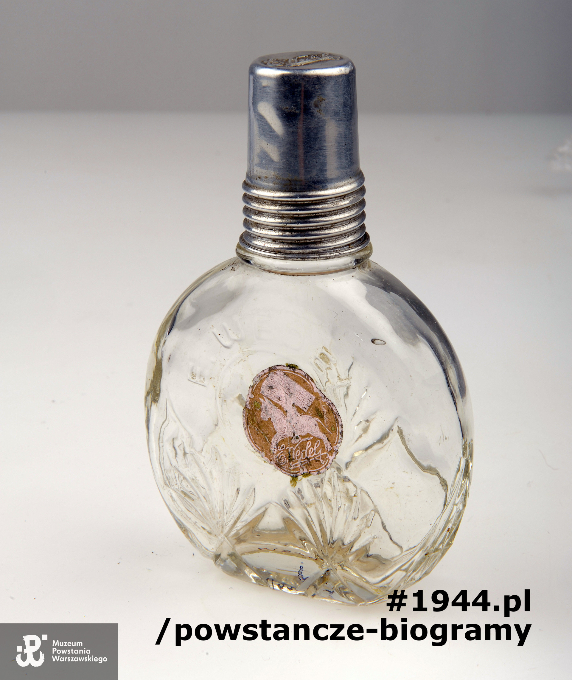 Buteleczka szklana z wytłoczonym napisem: E.Wedel, z aluminiowa zakrętką będąca także dozownikiem. Na środku butelki naklejona etykieta firmowa z napisem: E. Wedel, przedstawiająca rycerza w zbroi na koniu trzymającego tabliczki czekolady. Buteleczka ta znajdowała się przy zwłokach Janiny Sarneckiej (zginęła leżąc ranna podczas bombardowania szpitala). Do butelki dołączono w celach identyfikacyjnych kartkę z danymi poległej. Ze zbiorów Muzeum Powstania Warszawskiego - muzealia artystyczno-historyczne, sygn. MPW-M/2370 (P/5791/07). Obiekt prezentowany na wystawie czasowej "1000 Pamiątek" (2017/2018 r.)