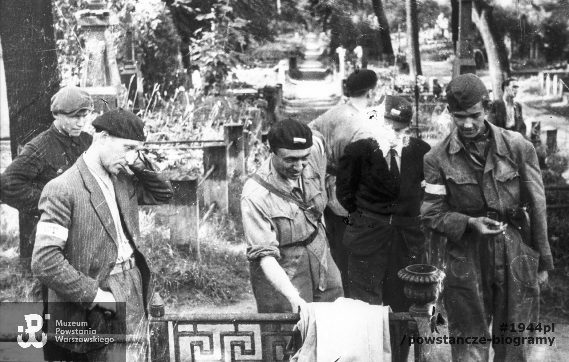 Fotografia z Powstania Warszawskiego. Wola. Godzina "W". Zbiórka powstańców z plutonu "Agaton" Batalionu "Pięść" na terenie cmentarza ewangelicko-augsburskiego. Stoją od lewej: (NN), kpr. Czesław Wegner "Bartek", st. strz. Kazimierz Piechotka "Jacek", strz. Zygmunt Skrobański "Blikle", strz. (NN) "Adam", strz. Piotr Woyzbun "Janusz". Na dalszym planie widoczne nagrobki cmentarza w kierunku północnym.Autorem zdjęcia jest Stefan Bałuk. Fot. ze zbiorów Muzeum Powstania Warszawskiego, sygn. MPW-IH/3417