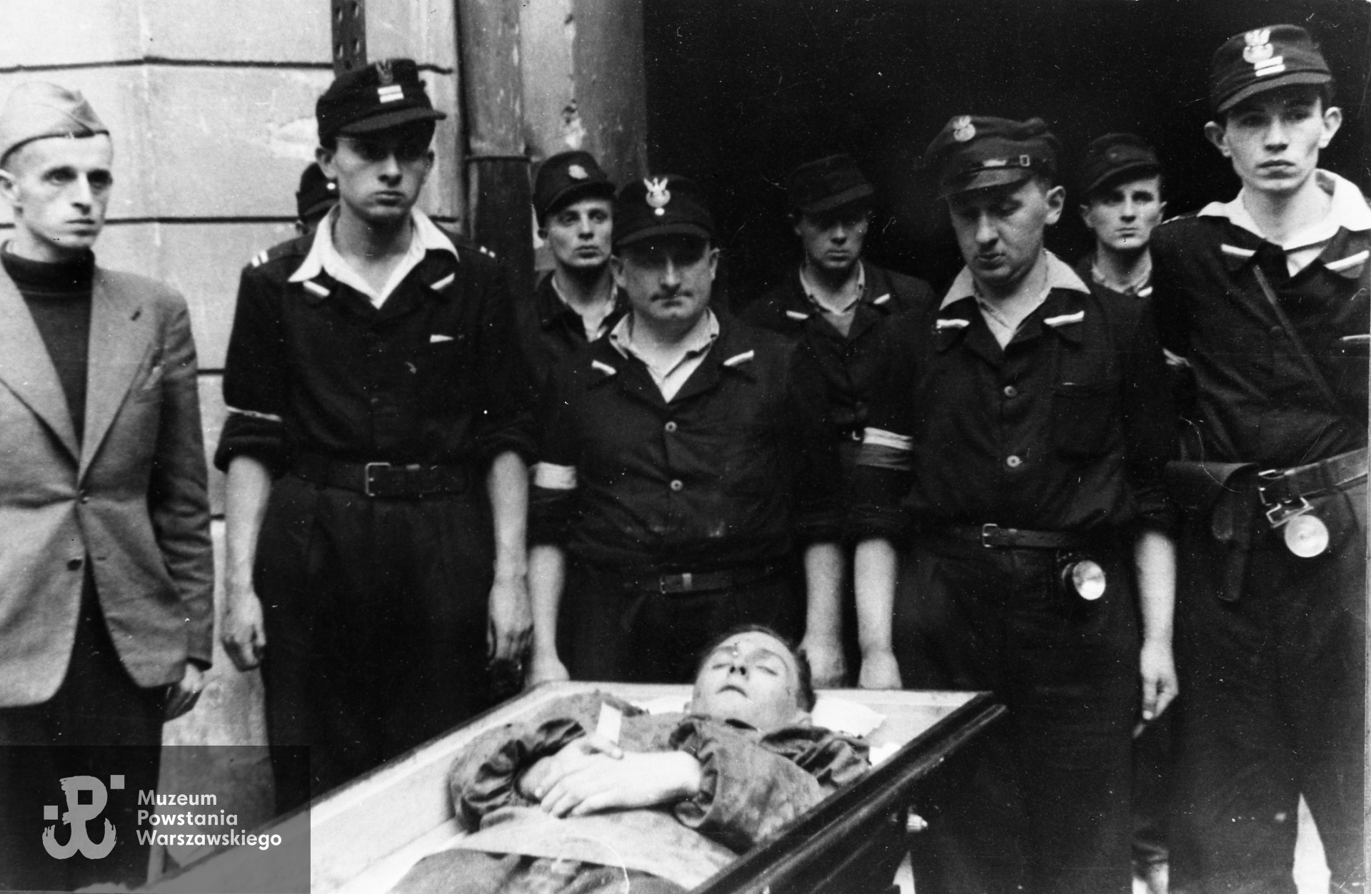Fotografia z Powstania Warszawskiego. Śródmieście Północne, ulica Chmielna. Żołnierze 1. kompanii Zgrupowania "Gurt" przy trumnie kpr. pchor. Jerzego Romana Graczyka "Roman", dowódcy plutonu 153, który zginął w ataku na restaurację "Żywiec". Od lewej por. Tadeusz Henryk Gruszczyński "Poraj". Fot. ze zbiorów Muzeum Powstania Warszawskiego, sygn.MPW-IH/5843