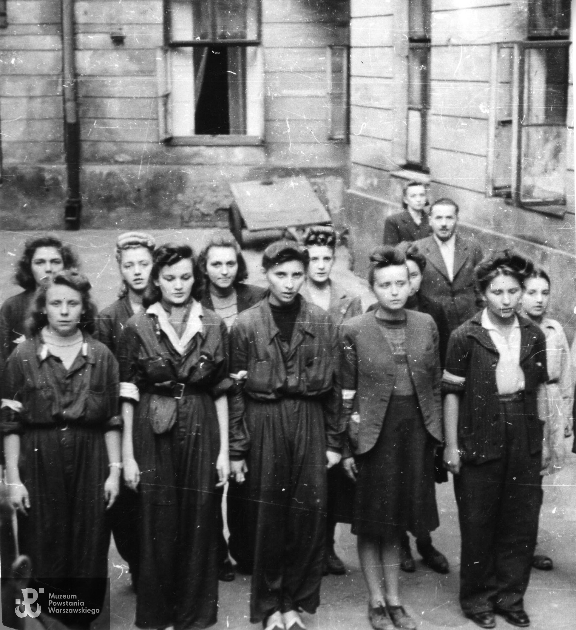 Fotografia z Powstania Warszawskiego. Śródmieście Południowe, ul. Książęca. Barykada z samochodów przecinająca ulicę. Od lewej: pchor. Lech Pudłowski "Leszek", ppor. Henryk Bigajski "Potocki", Daniela Białowąs "Nutka", Wacława Sutowska "Aćka". Stoi pchor. "Korwin". W głębi widoczny mur posesji Książęca 10. Fot. ze zbiorów Muzeum Powstania Warszawskiego, sygn. MPW-IH/5919