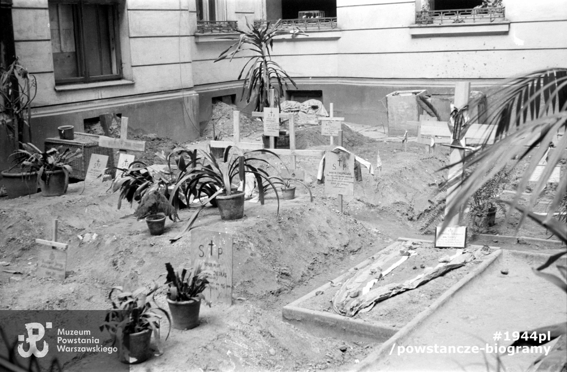 Fotografia z okresu Powstania Warszawskiego przedstawiająca tymczasowy cmentarz utworzony na podwórzu kamienicy przy ul. Brackiej 23, gdzie pochowano por. Juliana Głowackiego „Ogórka”. Widoczne także tabliczki nagrobne: Wanda Chłopkówna „Wandzia”, Stanisław Silkiewicz „Szary”, Ireneusz Pietras „Wierzbicki”. Autorem zdjęcia jest Sylwester „Kris" Braun. Fot. ze zbiorów ikonograficznych Muzeum Powstania Warszawskiego, przekaz z MHW