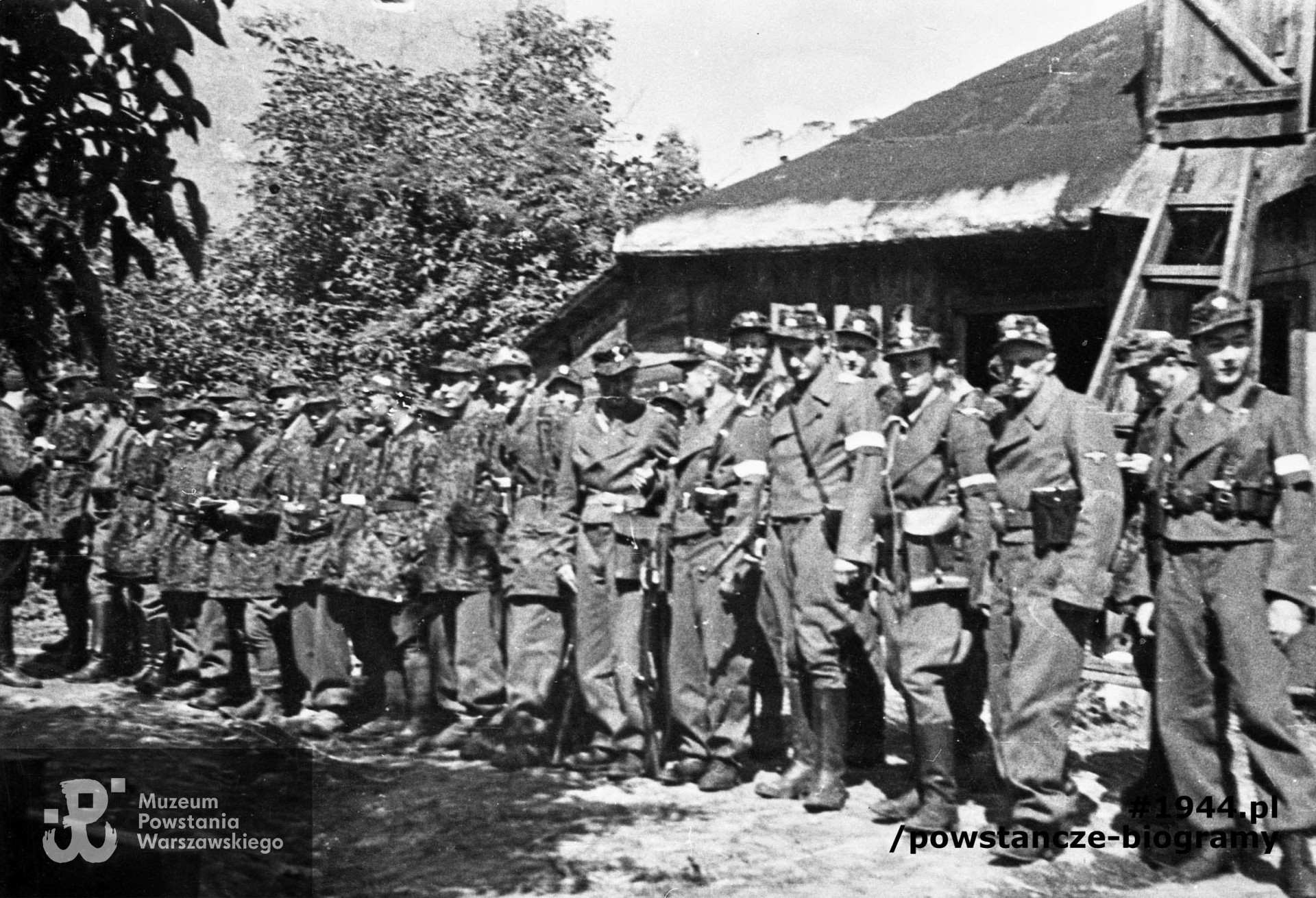 Fotografia z Powstania Warszawskiego. Wola. Żołnierze Kolegium "A" Kedywu OW AK w ogrodzie RGO - ul. Okopowa 41. Stoją od lewej: Aleksander Kabański "Brzozowski" (bokiem), trzeci - Jan Bagiński "Socha" (w berecie), czwarty - Zygmunt Siennicki  (Sieliński) "Bor" , ósmy - Józef Tomaszewski "Klemens". Dziewiąty od prawej - Jerzy Krzymowski "Jodła" (twarz w cieniu), czwarty od prawej- Jan Kulczycki "Argos" (w długich butach). Fot. zbiorów Muzeum Powstania Warszawskiego, sygn. MPW-IN/3643