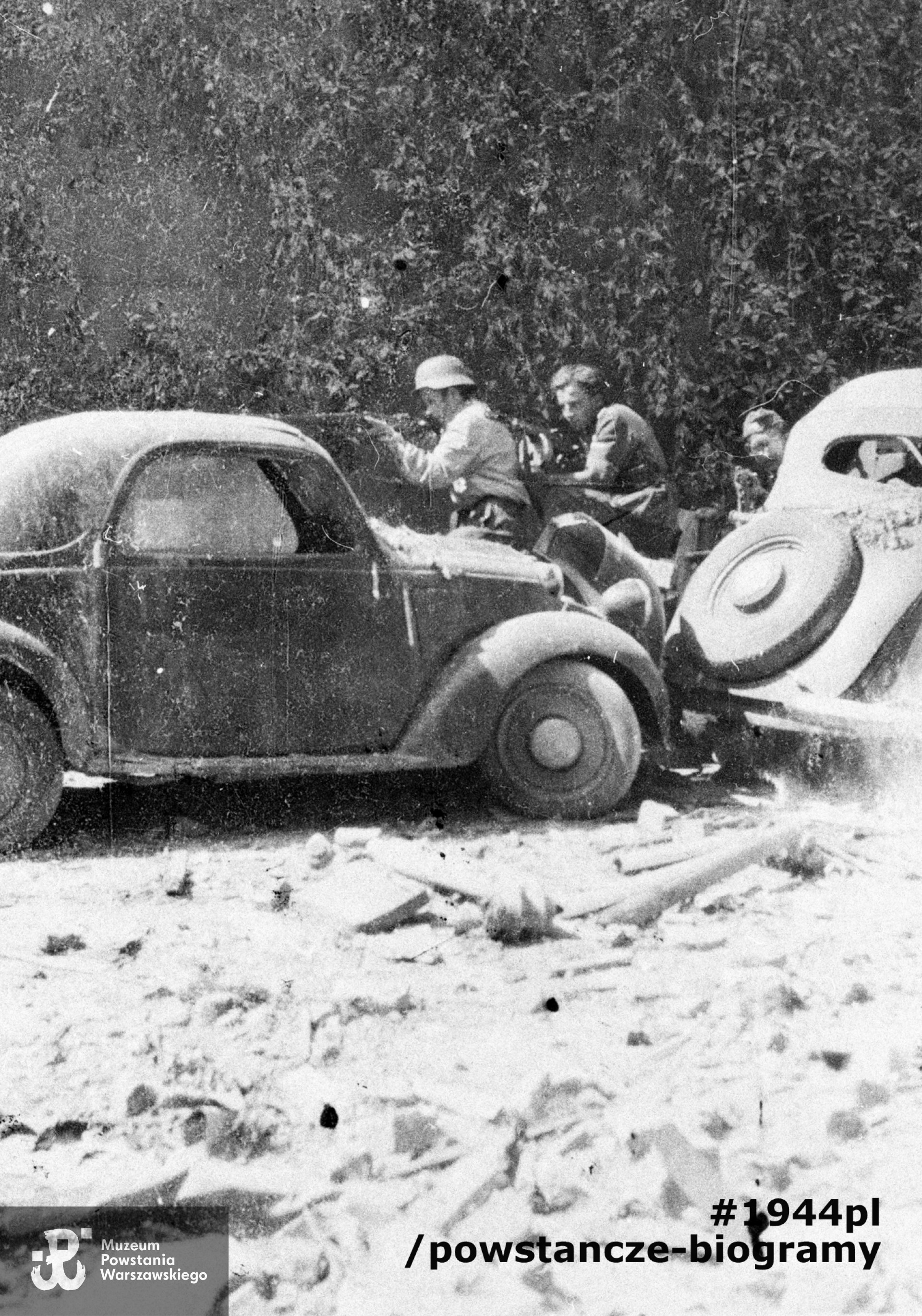 Fotografia z Powstania Warszawskiego. Ujęcie pozowane. Śródmieście Północne. Powstańcy z 2 kompanii Zgrupowania "Bartkiewicz" ukryci za samochodami stojącymi w bocznej uliczce wiodącej na dziedziniec Towarzystwa Kredytowego Ziemskiego przy ul. Kredytowej 1 (podczas okupacji mieścił się tu Arbeitsamt). Od lewej: st. strz. Stefan Matyjaszkiewicz "Stefek" (w hełmie), kpr. Lotar Kozłowski "Olgierd" i st. strz. Waldemar Malinowski "Waldek". Fot. ze zbiorów Muzeum Powstania warszawskiego, sygn. MPW-IH/2681