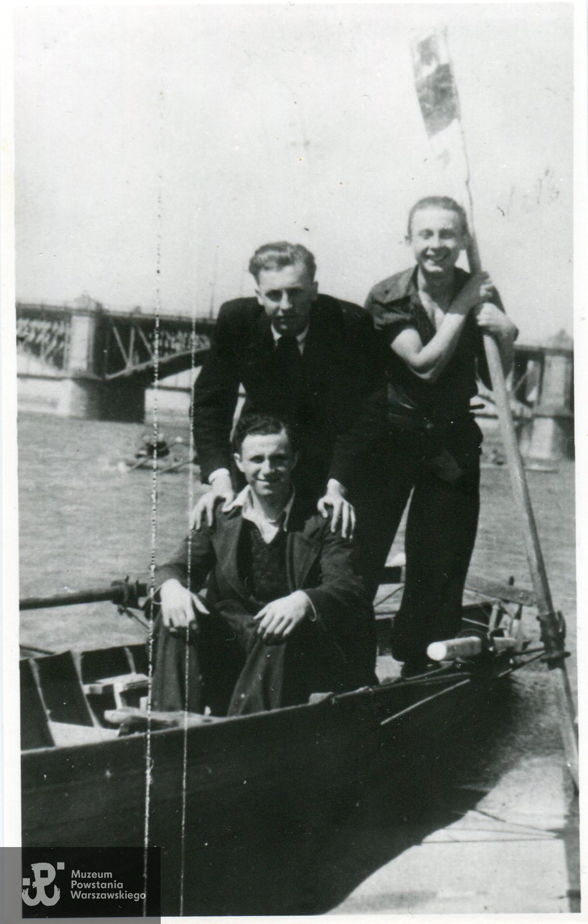 Fotografia wykonana w okresie okupacji niemieckiej, przed wybuchem Powstania Warszawskiego. Widok od strony Saskiej Kępy w kierunku mostów Poniatowskiego i średnicowego.  Na zdjęciu od lewej: siedzi Wiesław Gucman ps. Stefan, nad nim kolega NN, z wiosłem Edward Łopatecki ps. Młodzik. Fot. ze zbiorów rodzinnych, skan udostępnił p. Krzysztof Gucman, syn Powstańca
