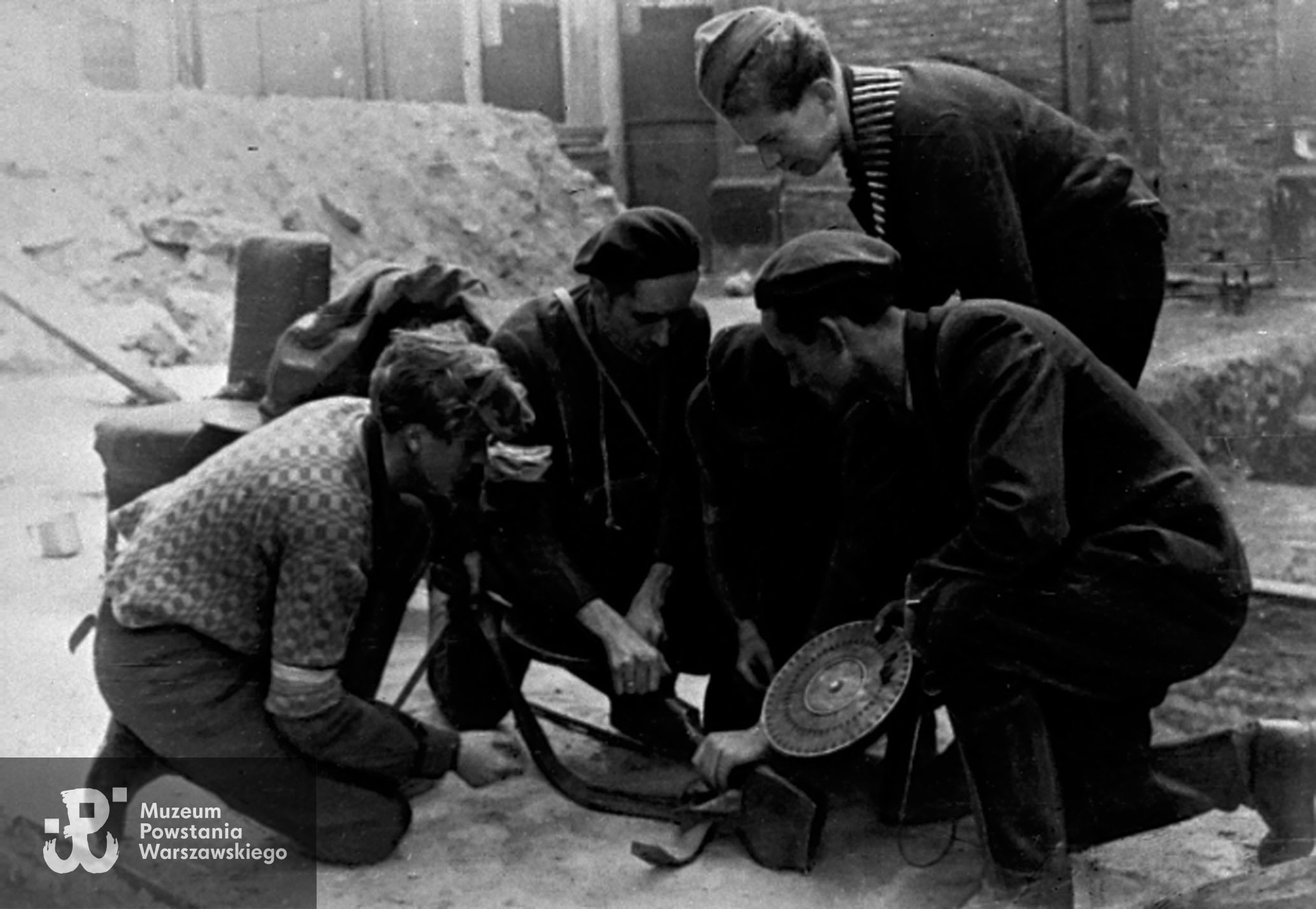 Fotografia z Powstania Warszawskiego autorstwa Bernarda Marwińskiego (PSW). Śródmieście Północne, ul. Żelazna. Grupa powstańców podczas nauki wymiany magazynku w sowieckim karabinie maszynowym DP wz. 1928. Zdjęcie zrobione prawdopodobnie na ulicy Żelaznej, ze zbiorów Muzeum Powstania Warszawskiego, sygn. MPW-IH/4278