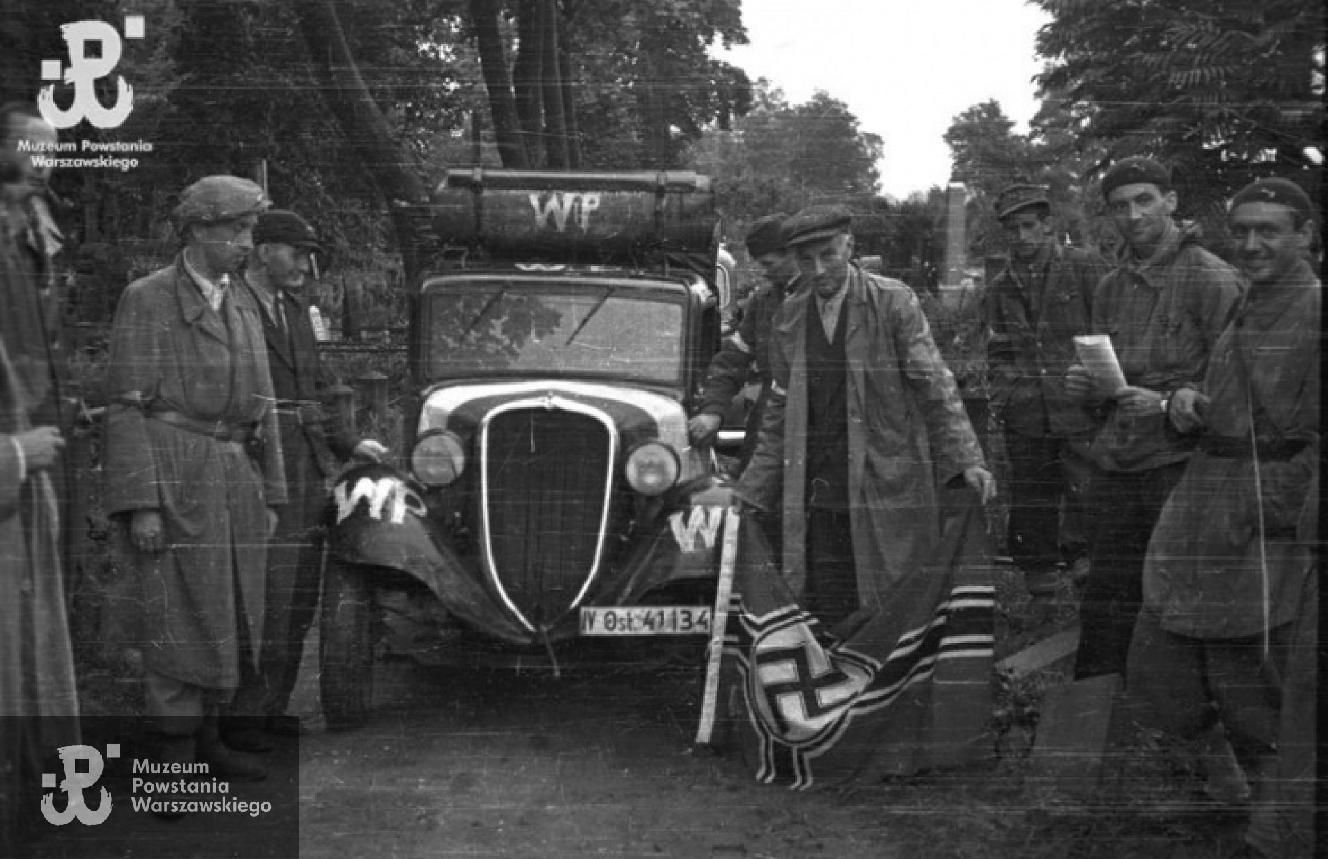 Mjr Alfons Kotowski "Okoń" demonstruje zdobytą hitlerowską flagę na terenie cmentarza ewangelicko-augsburskiego. Zdjęcie autorstwa Stefana Bałuka, ze zbiorów Fototeki MPW , sygnatura<a href=" http://www.1944.pl/galerie/fototeka/foto/7901/autor/126"> MPW-IS/127</a>