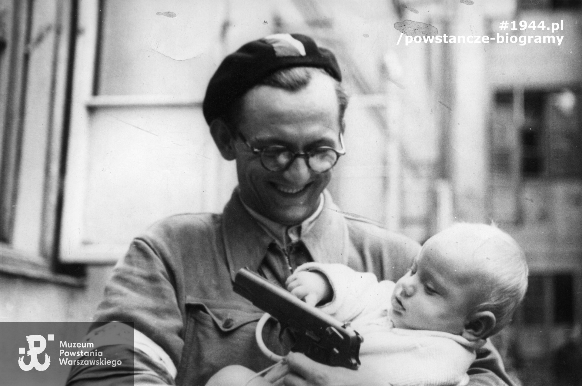 Fotografia z Powstania Warszawskiego autorstwa Wacława Żdżarskiego (PSW). Śródmieście Północne. Podporucznik Zygmunt Mikołaj Malinowski "Kruk", dowódca I plutonu Oddziału Osłony Kwatery Głównej pokazuje pistolet  trzymanemu na rękach rocznemu synowi Wiesławowi. Fot. ze zbiorów Muzeum Powstania Warszawskiego, sygn. MPW-IP/6017