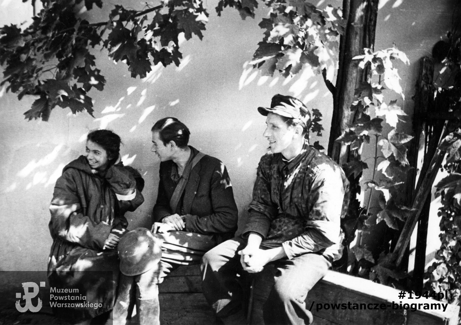 Fotografia z Powstania Warszawskiego. Powstańcy z batalionu "Czata 49" po ewakuacji kanałami ze Starówki odpoczywają na jednej z posesji przy ul. Wareckiej. Z lewej siedzi sanitariuszka "Iza" Izabella Wilbik, strz. "Ulatowski" - Jan Welt i strz. "Kowalski" - Tadeusz Roman. Fot. ze zbiorów Muzeum Powstania Warszawskiego, sygn. MPW-IK/1841