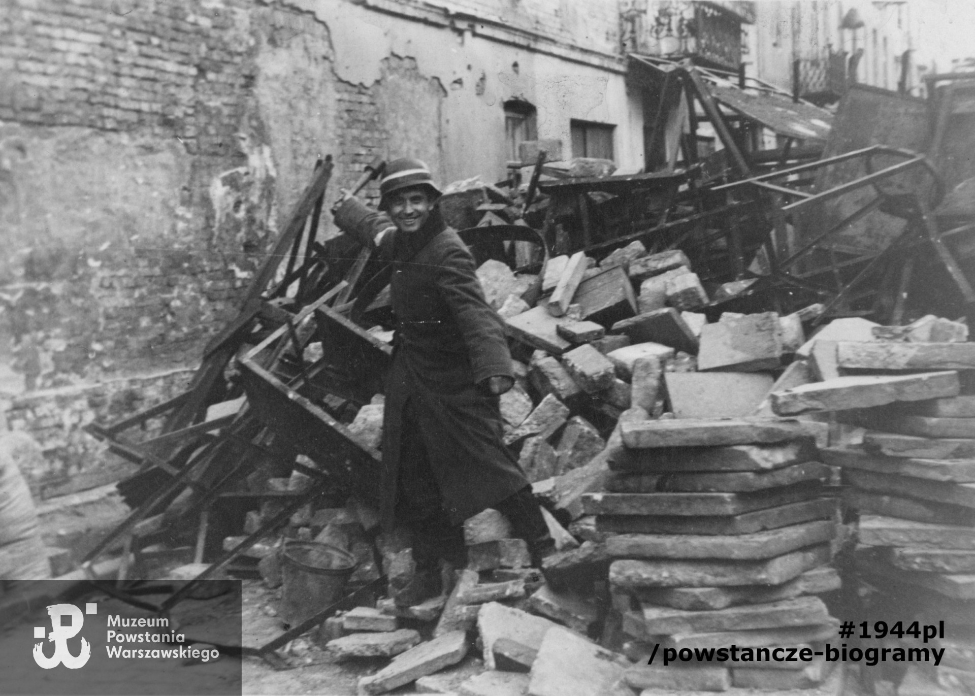 Fotografia pozowana przy jednej ze staromiejskich barykad. Alfons Milewczyk w hełmie powstańczym, trzymający w prawej ręce granat trzonkowy.  Fot. ze zbiorów Muzeum Powstania Warszawskiego, sygn. P/9079, dar p. Krzysztofa Jaworskiego
